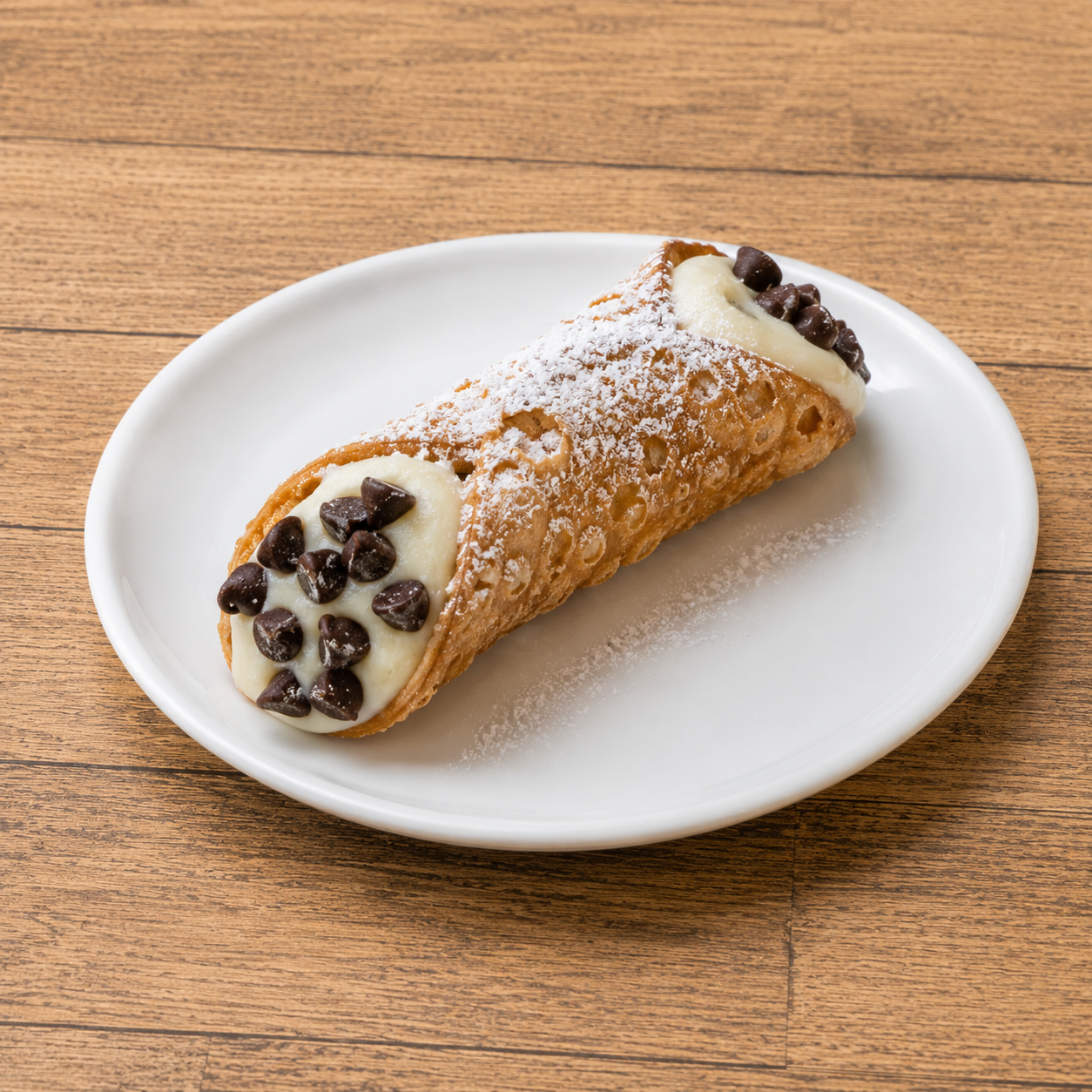 A cannoli pastry with ricotta filling, chocolate chips, and powdered sugar on a white plate.