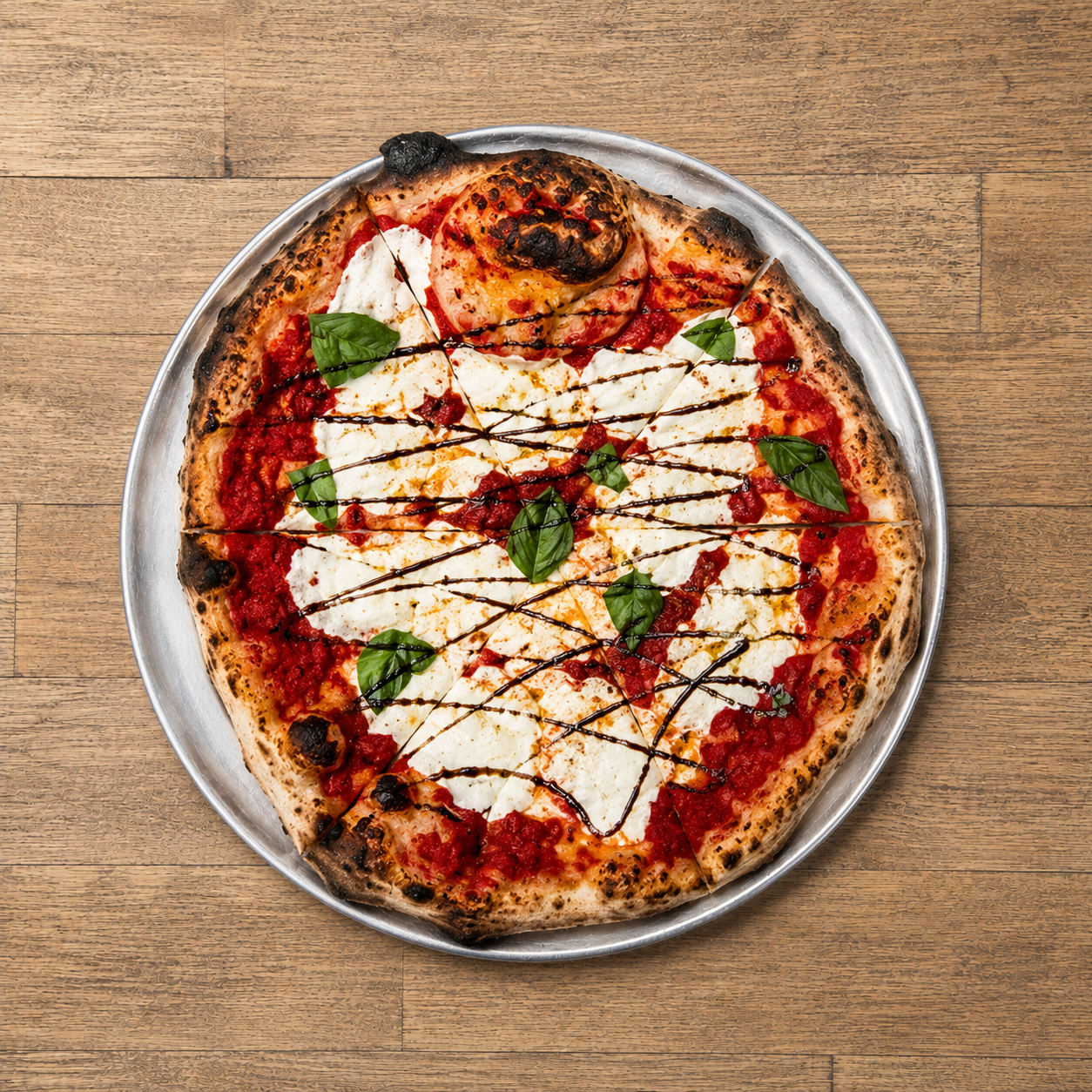 Margherita pizza with fresh basil leaves, drizzle of balsamic glaze, and dollops of mozzarella cheese on a wooden table.