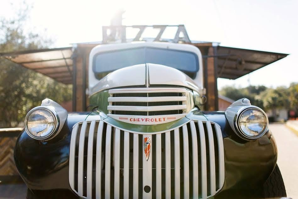 Front view of a vintage black Chevrolet truck with a large vertical grille and round headlights, parked outdoors in bright sunlight.