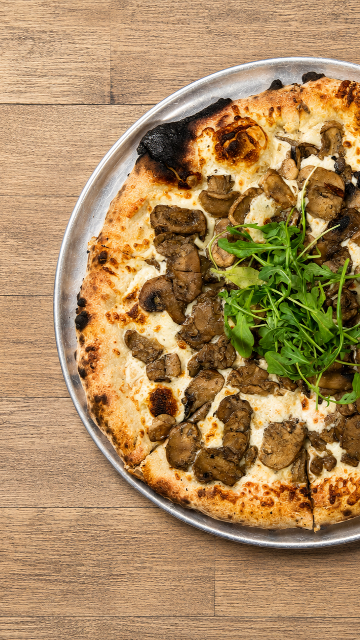 Pizza with mushrooms, cheese, and arugula on top served on a metal tray