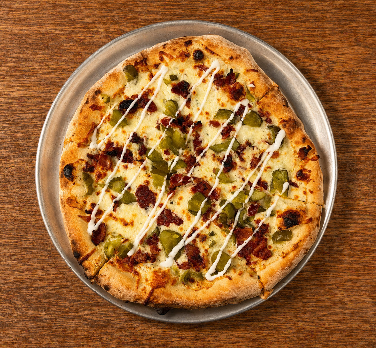 Pizza with cheese, bacon, and green peppers on a silver tray on a wooden table.
