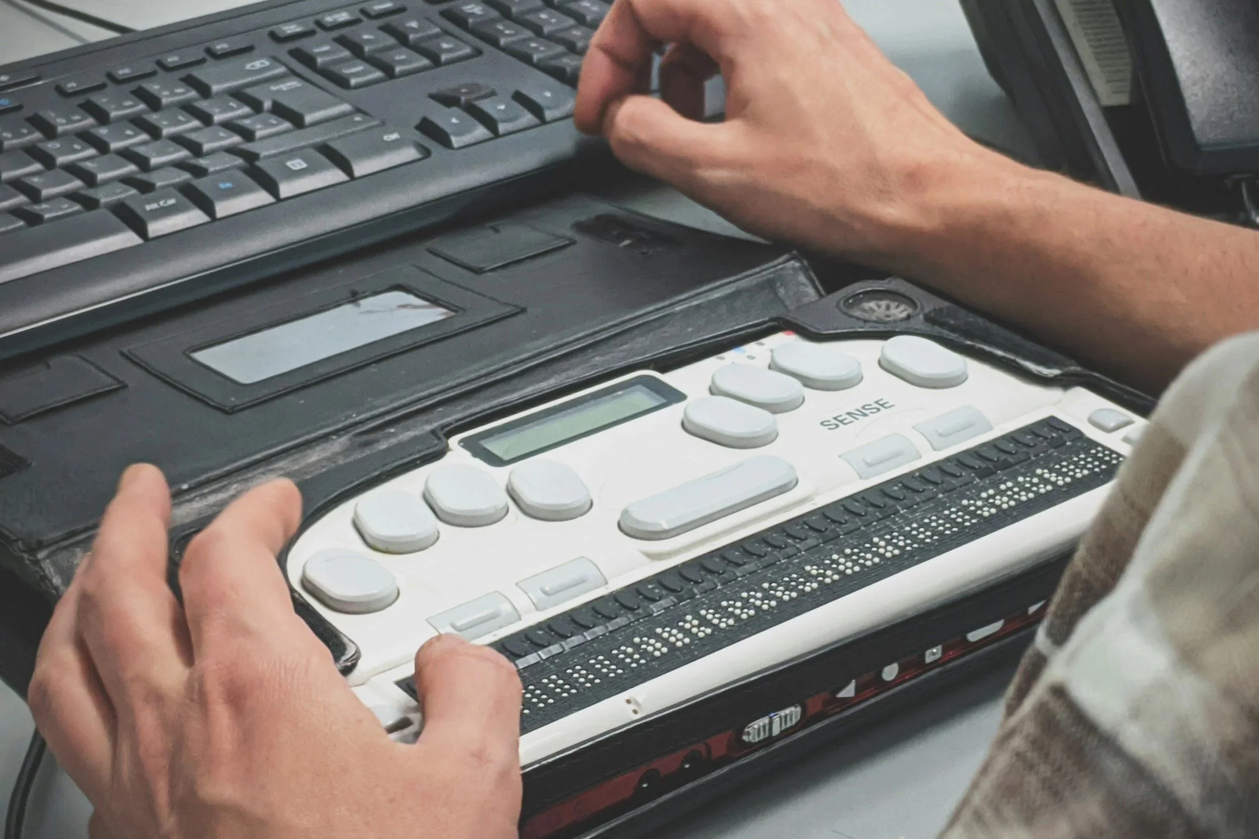 A person is using a refreshable Braille display connected to a computer keyboard