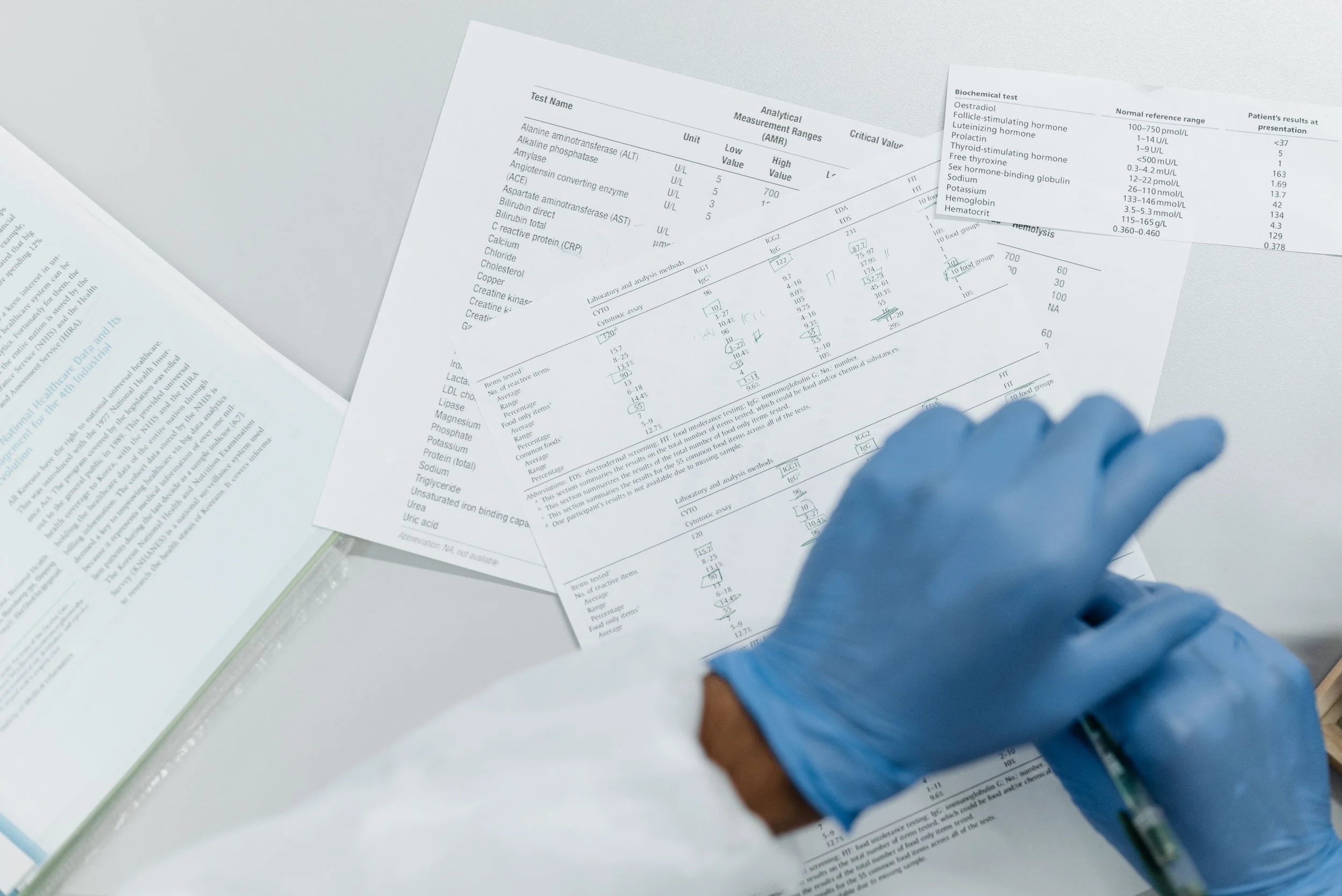 A person in blue gloves reviewing laboratory test results and biochemical measurement reports on white paper sheets on a white surface.