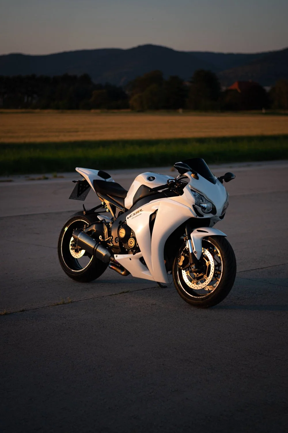 Weiße Sportmotorrad auf einer leeren Straße bei Sonnenuntergang mit Berg- und Baumhintergrund.