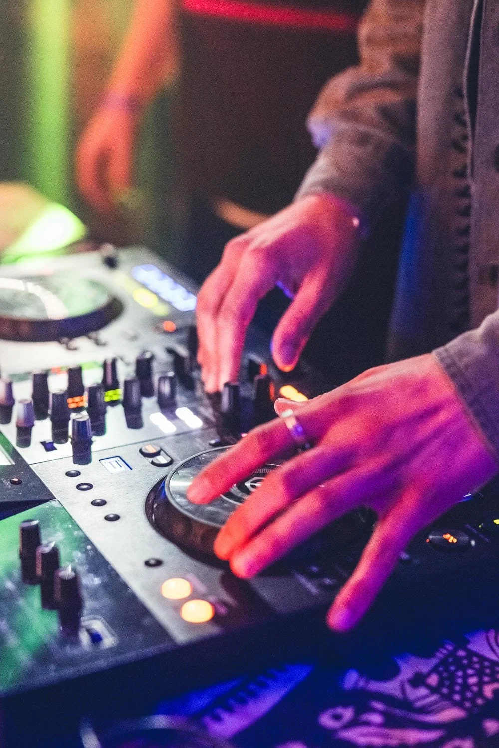 Nahaufnahme von einem DJ, der an einem Mischpult auflegt, mit bunten Lichtern und Steuerknöpfen.