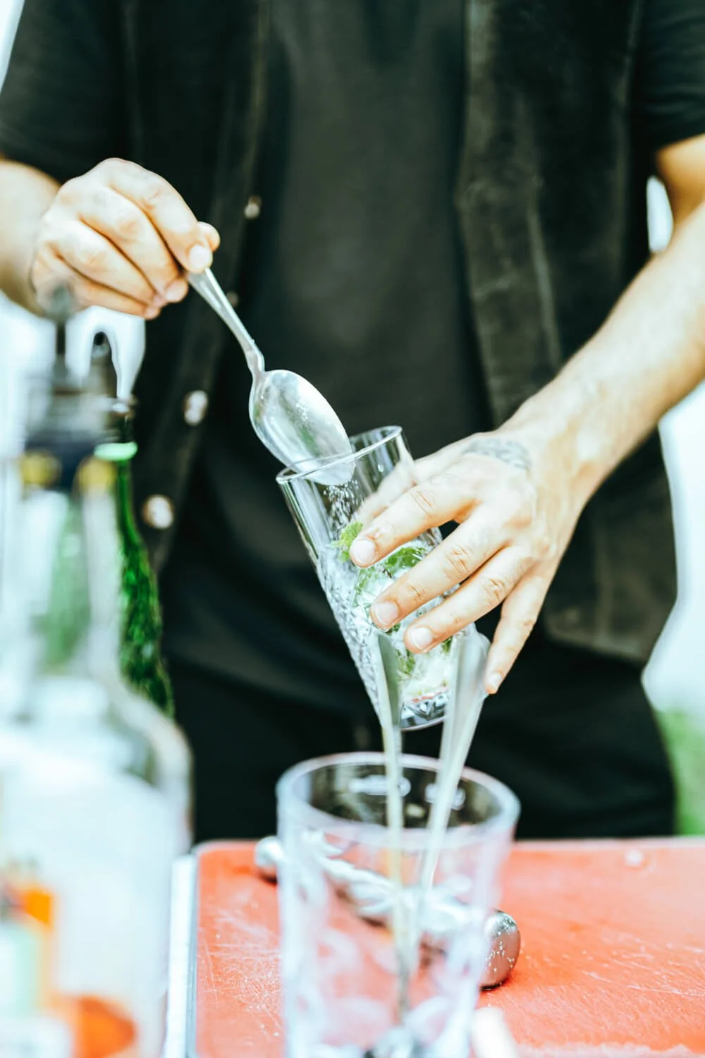 Person gießt Wasser in ein Glas mit Minzblättern und Eis.