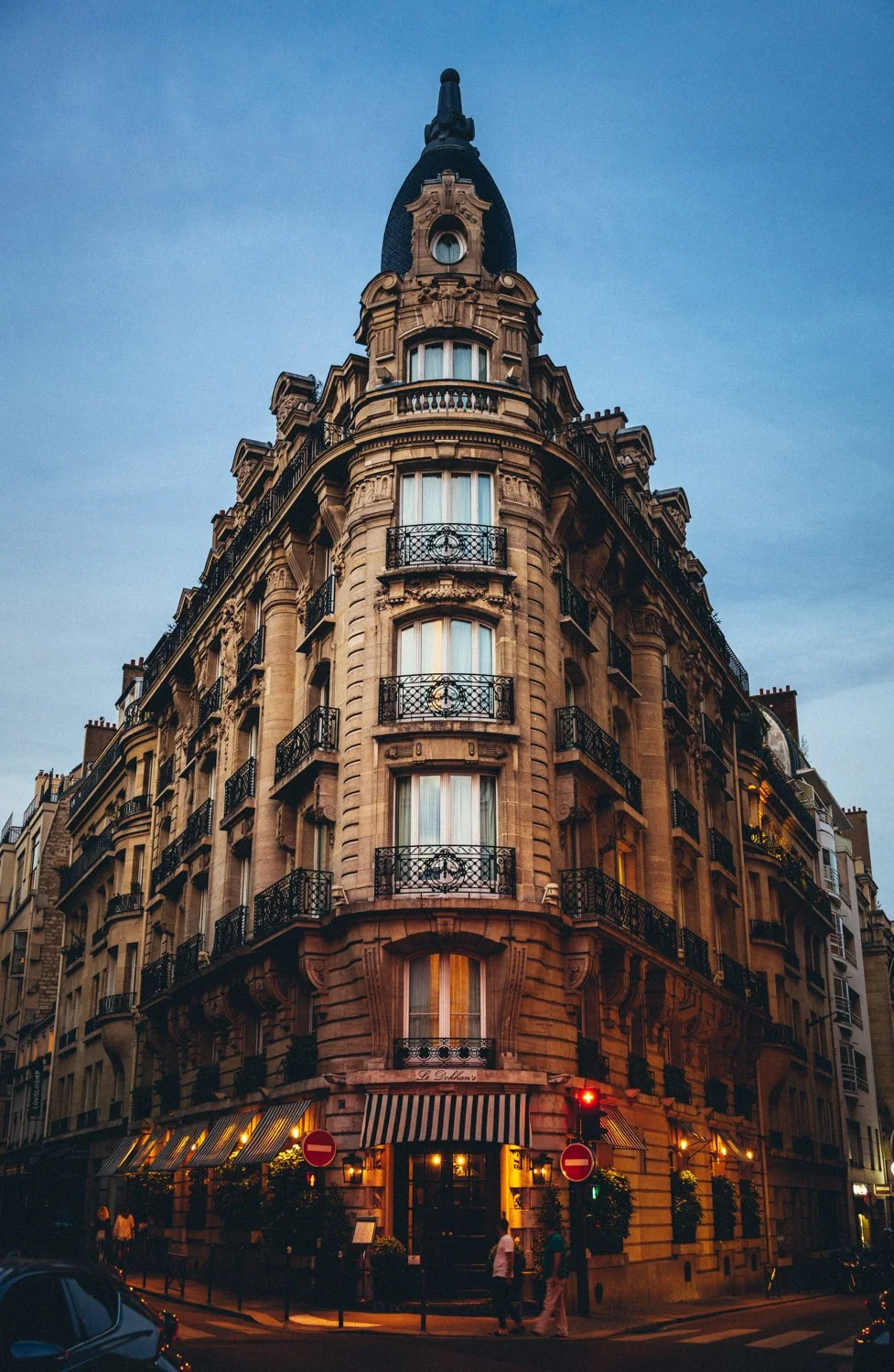 Ein historisches Gebäude in Paris mit mehreren Etagen, Balkonen und einer markanten Dachspitze, bei Dämmerung.