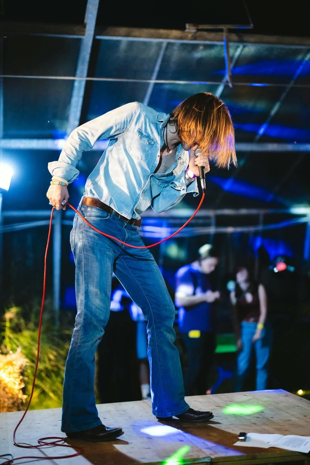 Ein junger Mann im Jeans-Look singt mit einem Mikrofon auf einer Bühne bei einer Veranstaltung.