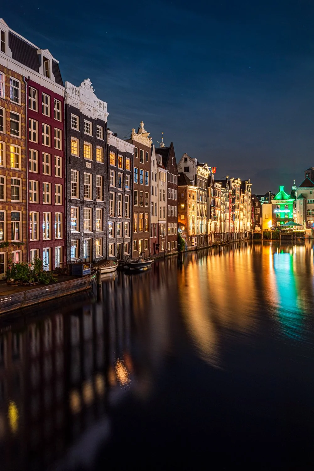 Bunte historische Häuser entlang eines Kanals bei Nacht mit Lichtern, die sich im Wasser spiegeln, in einer Stadt Europas.