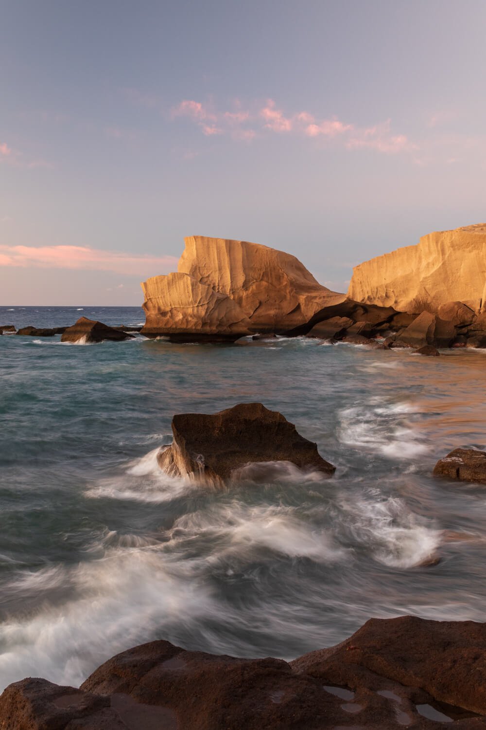 Felsformationen am Meer bei Sonnenuntergang mit Wellen, die gegen die Steine schlagen