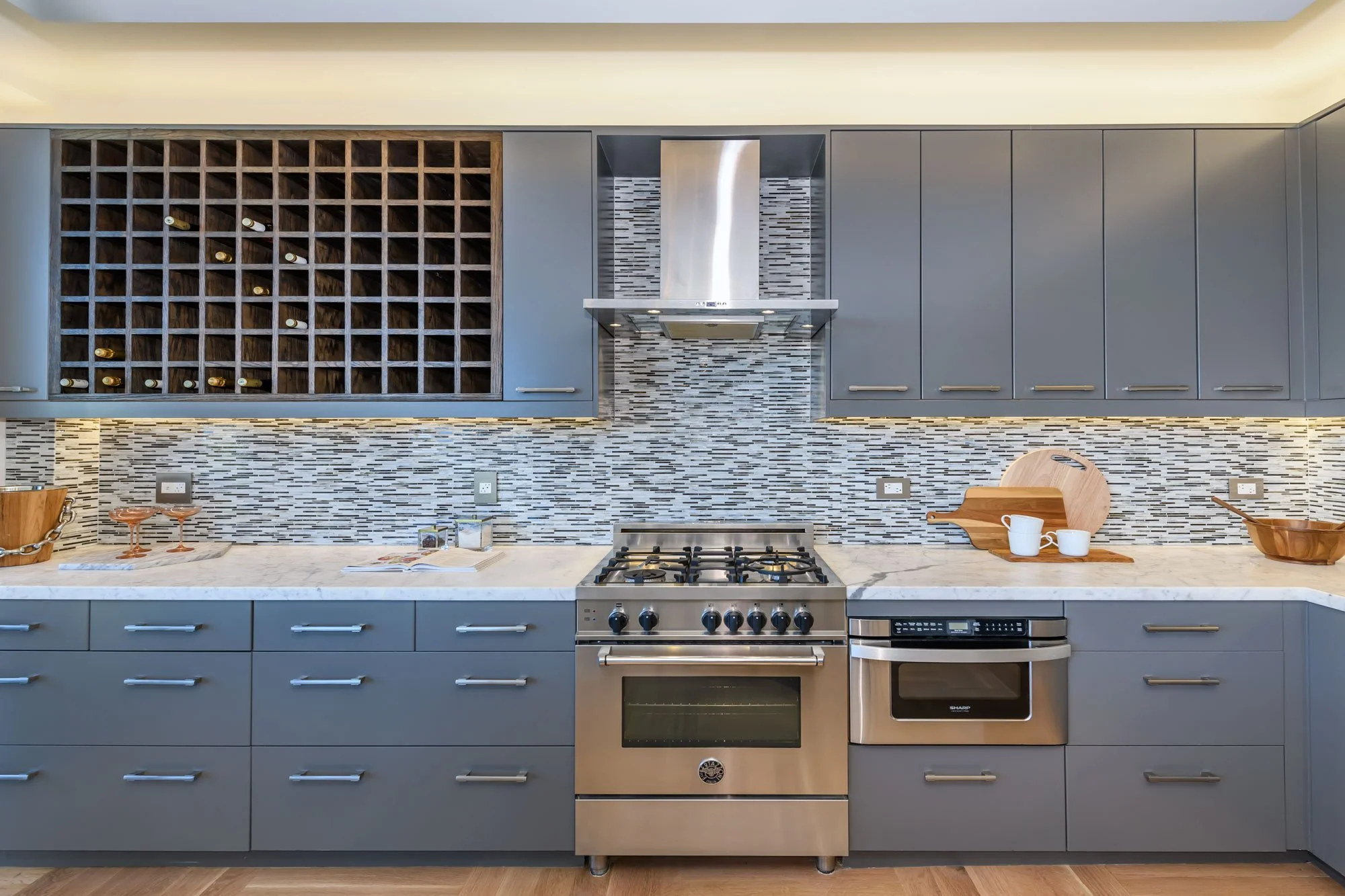 Modern kitchen with blue cabinets, marble countertop, stainless steel oven and range, wine rack, decorative backsplash, and kitchen items on the counter.