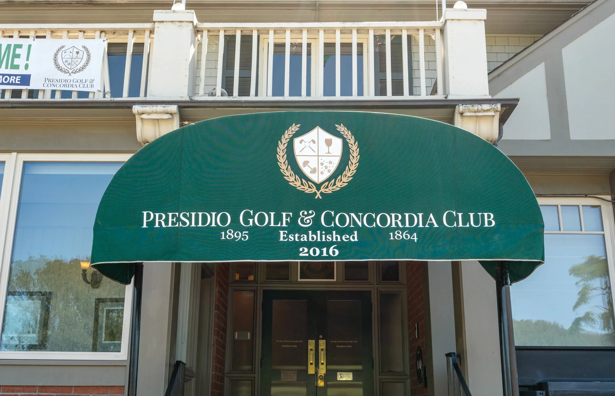 Entrance of Presidio Golf & Concordia Club with a green awning displaying the club's name, founding year 1895, incorporation year 1864, and established year 2016, featuring a shield emblem with golf clubs, a wine glass, a handshake, and stars.