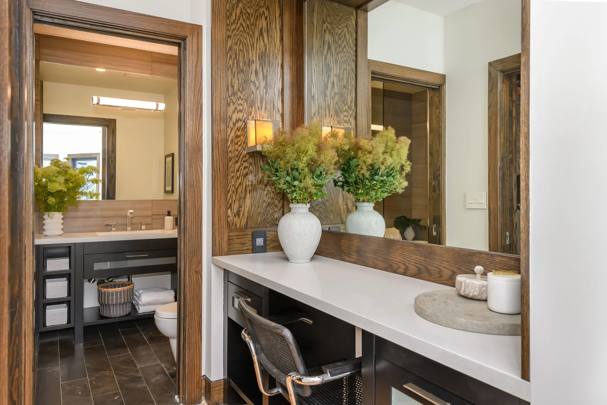 Bathroom with wooden framing, a large mirror, and a vanity area with decorative vases and flowers.