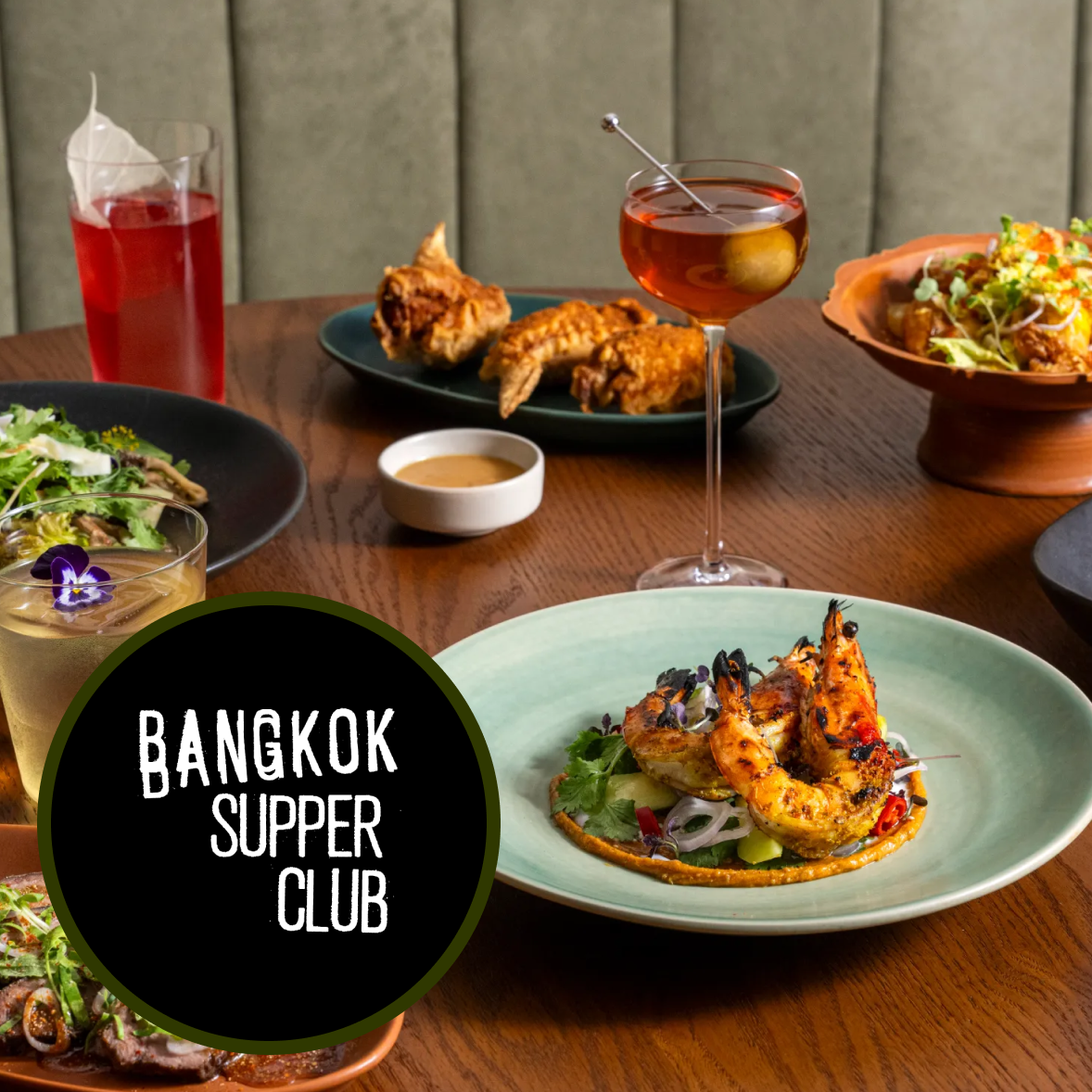 A table with various Asian dishes, including grilled shrimp, fried chicken, salad, and a cocktail, with a Bangkok Supper Club logo in the foreground.