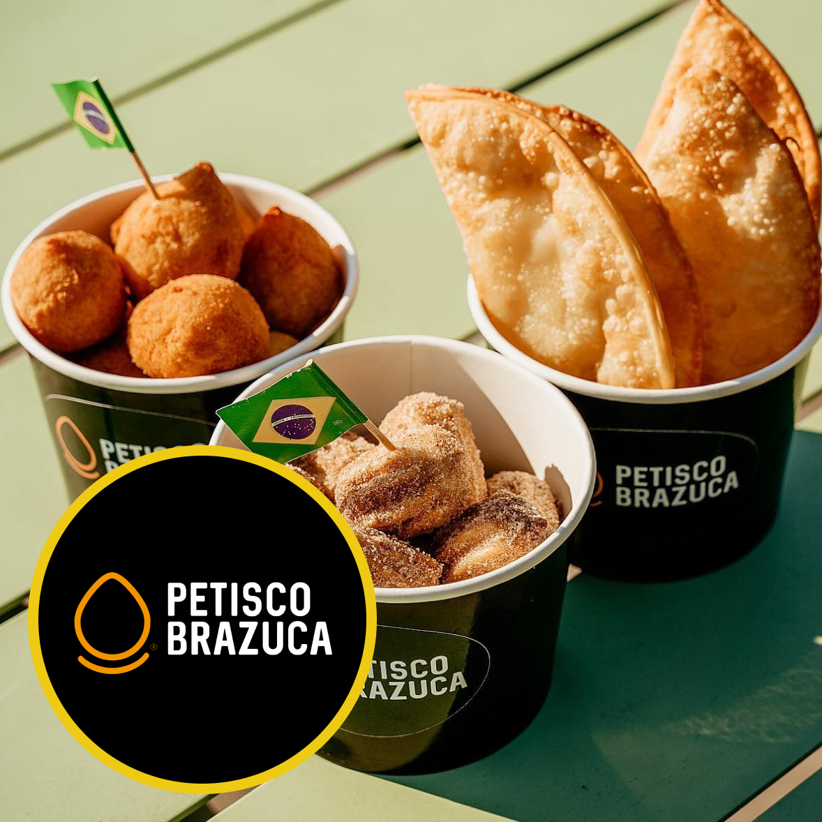 A bowl of fried Buzza balls with a dollop of sauce on one of them, placed on a wooden surface, with a Petisco Brazuca logo in the corner.