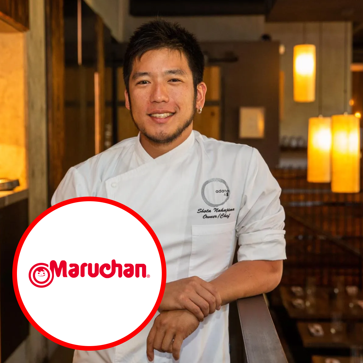 A chef wearing a white uniform smiling in a restaurant with warm lighting, with a large Maruchan logo overlayed on the lower left corner.