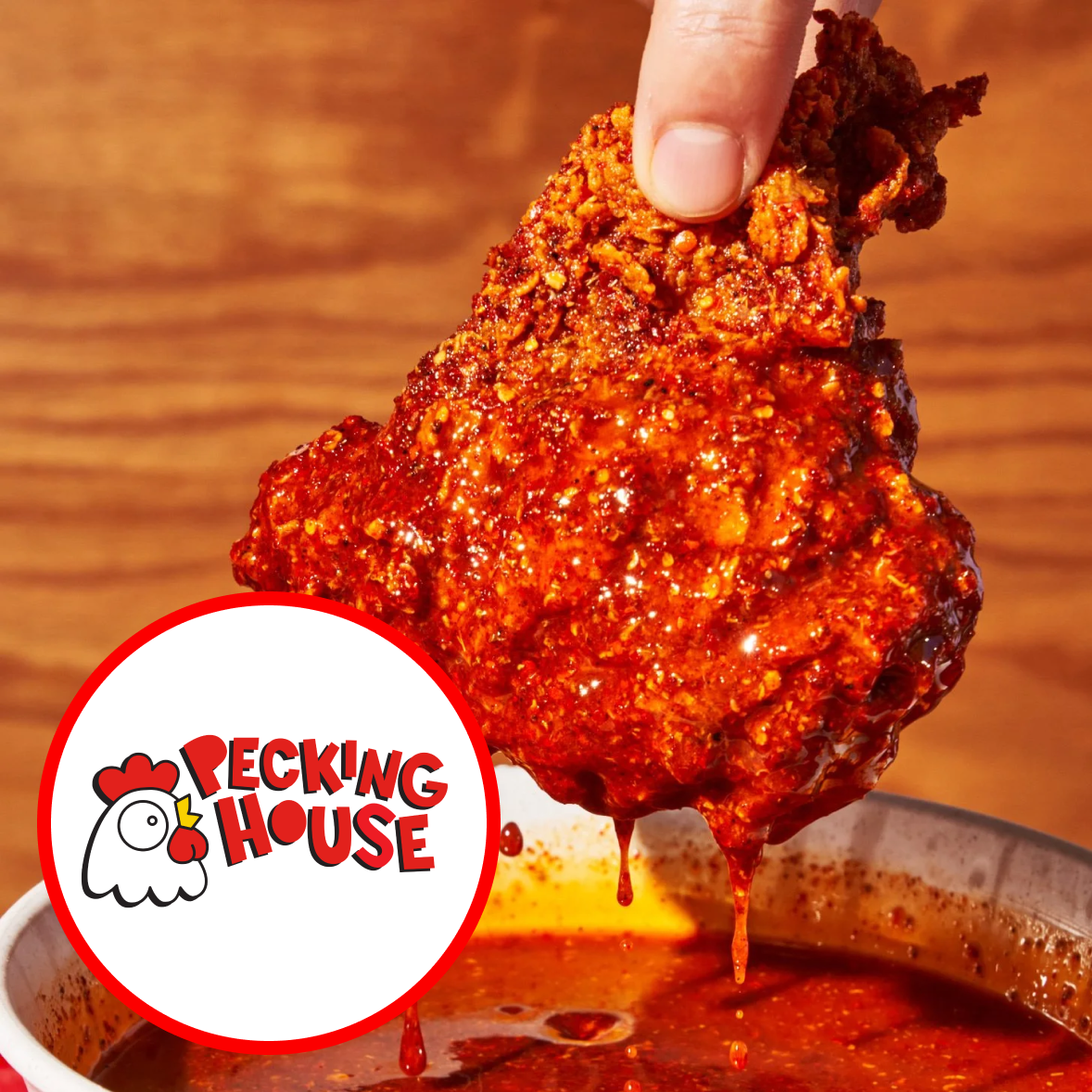 Close-up of a hand holding a spicy glazed chicken wing over a bowl of dipping sauce, with the Recking House logo in the foreground.