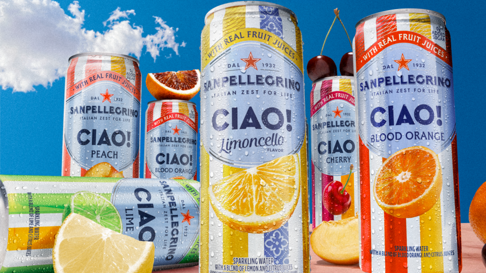 Variety of Sanpellegrino Ciao! flavored fruit juice cans, including peach, blood orange, lemon, cherry, and orange, with fresh fruit slices and a blue sky background.