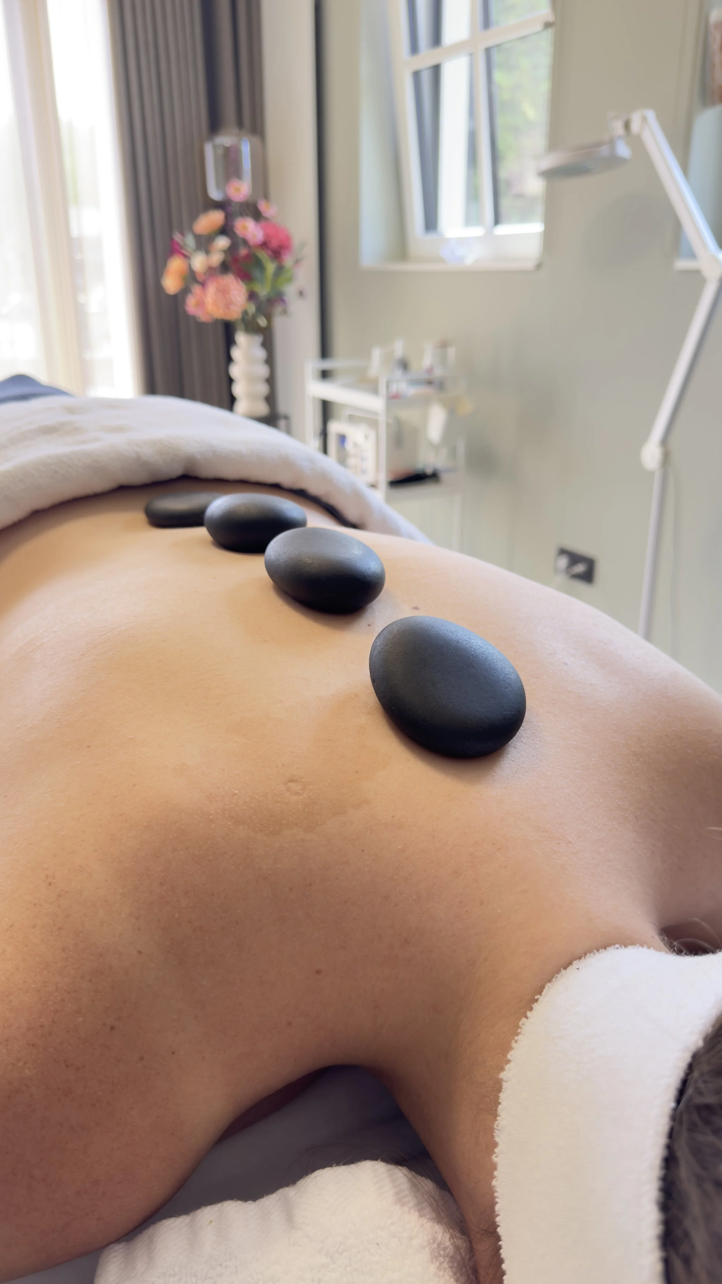 Een klant ligt op een massagetafel met vier zwarte hot stones op de rug, in een rustgevende salon.