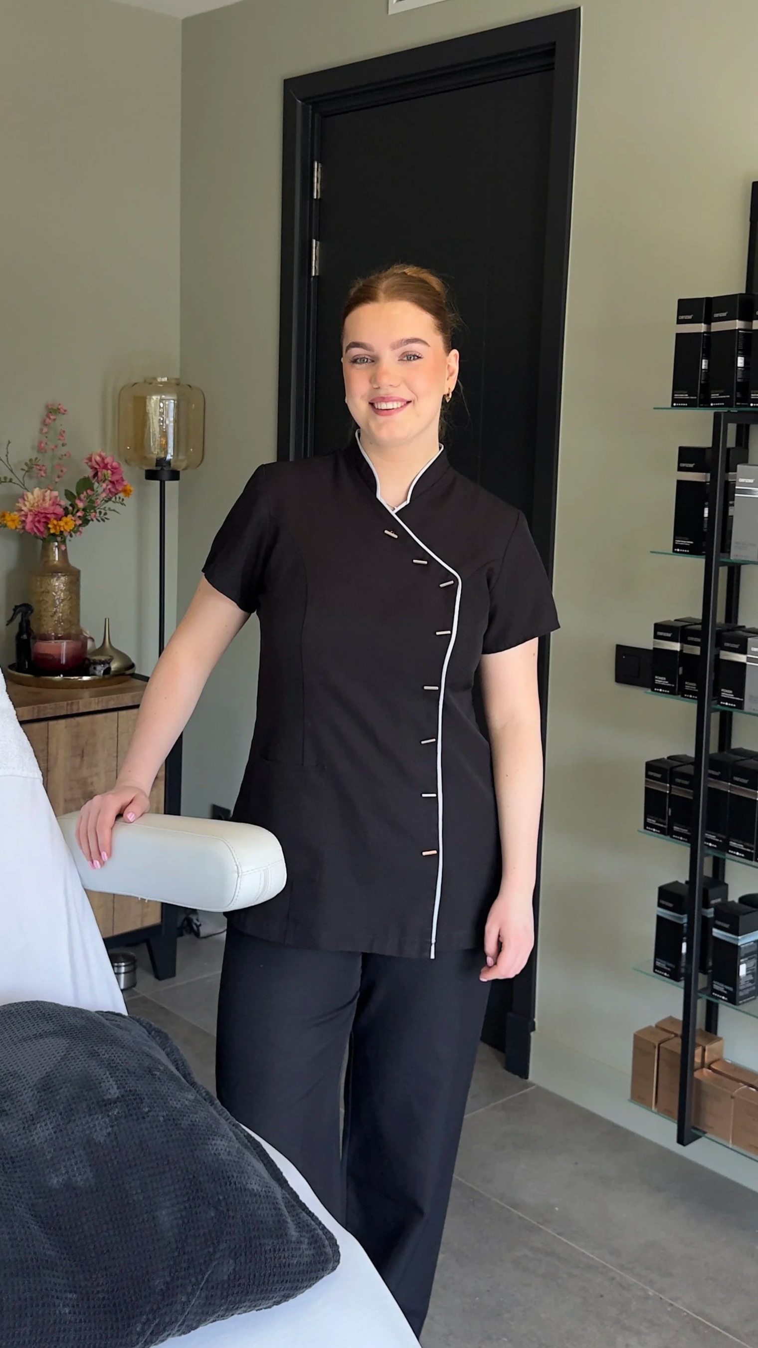 Julia Wijnen in zwart uniform staat in haar salon met zwarte rekken, glimlachend naar de camera.