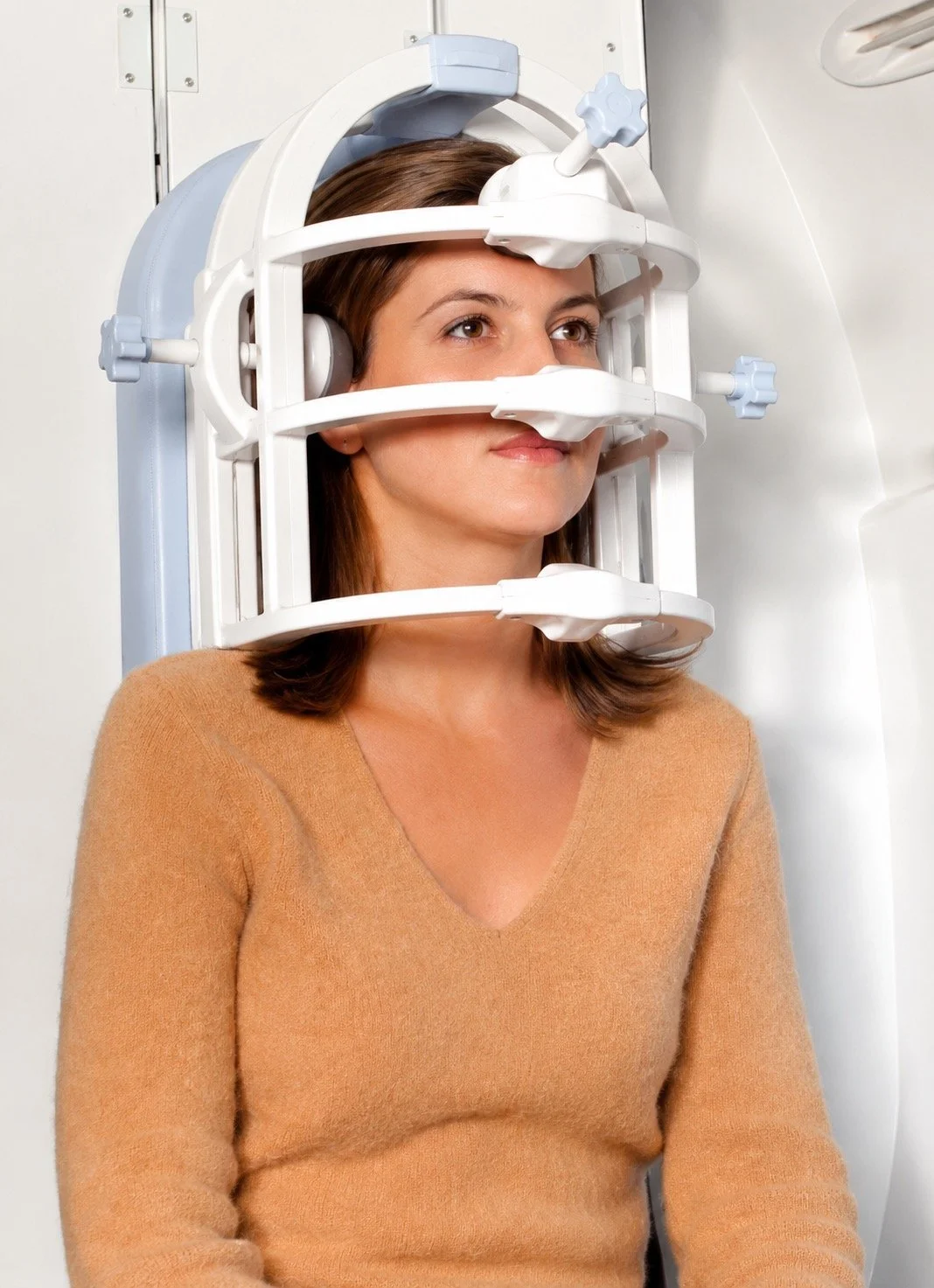 A woman undergoing a medical imaging procedure, lying still with a scanner around her head.