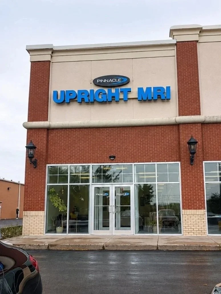 Exterior of Pinnacle UPRIGHT MRI clinic with a brick facade, glass entrance, and blue signage