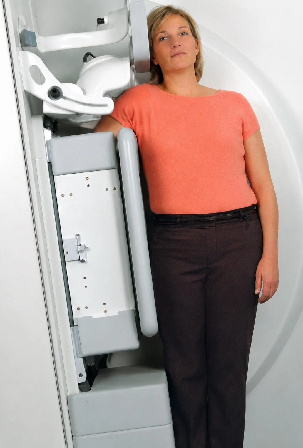 Woman undergoing a medical imaging scan, standing beside a large white medical machine.
