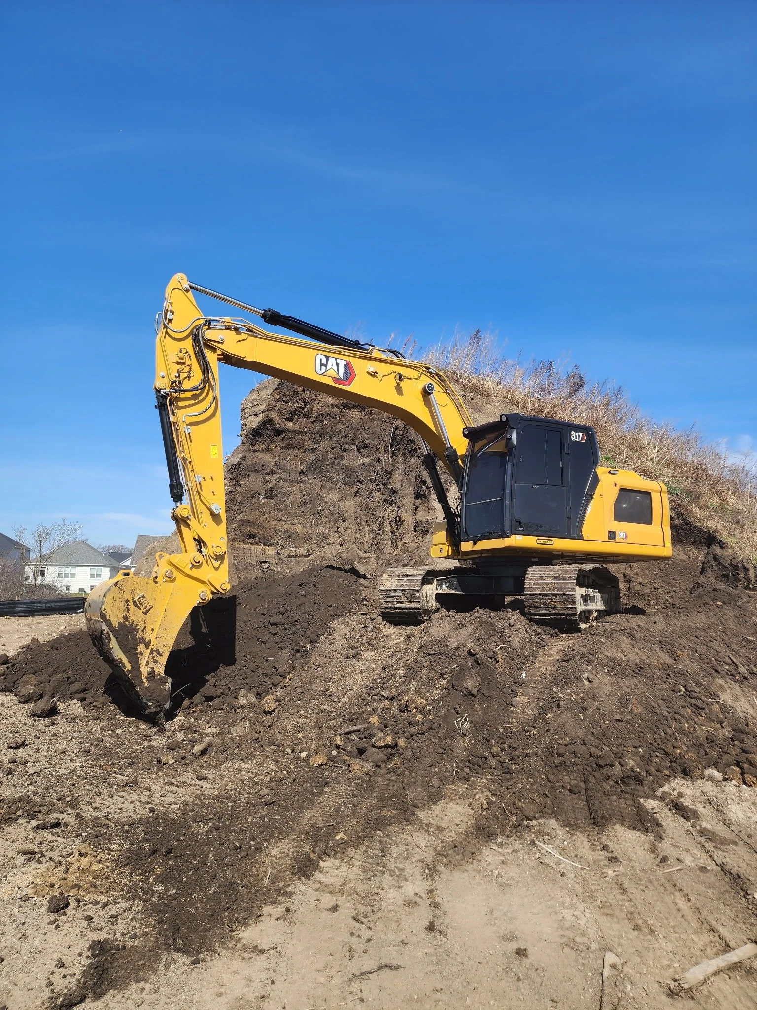 Yellow Caterpillar excavator digging up dirt at a construction site with blue sky in the background.