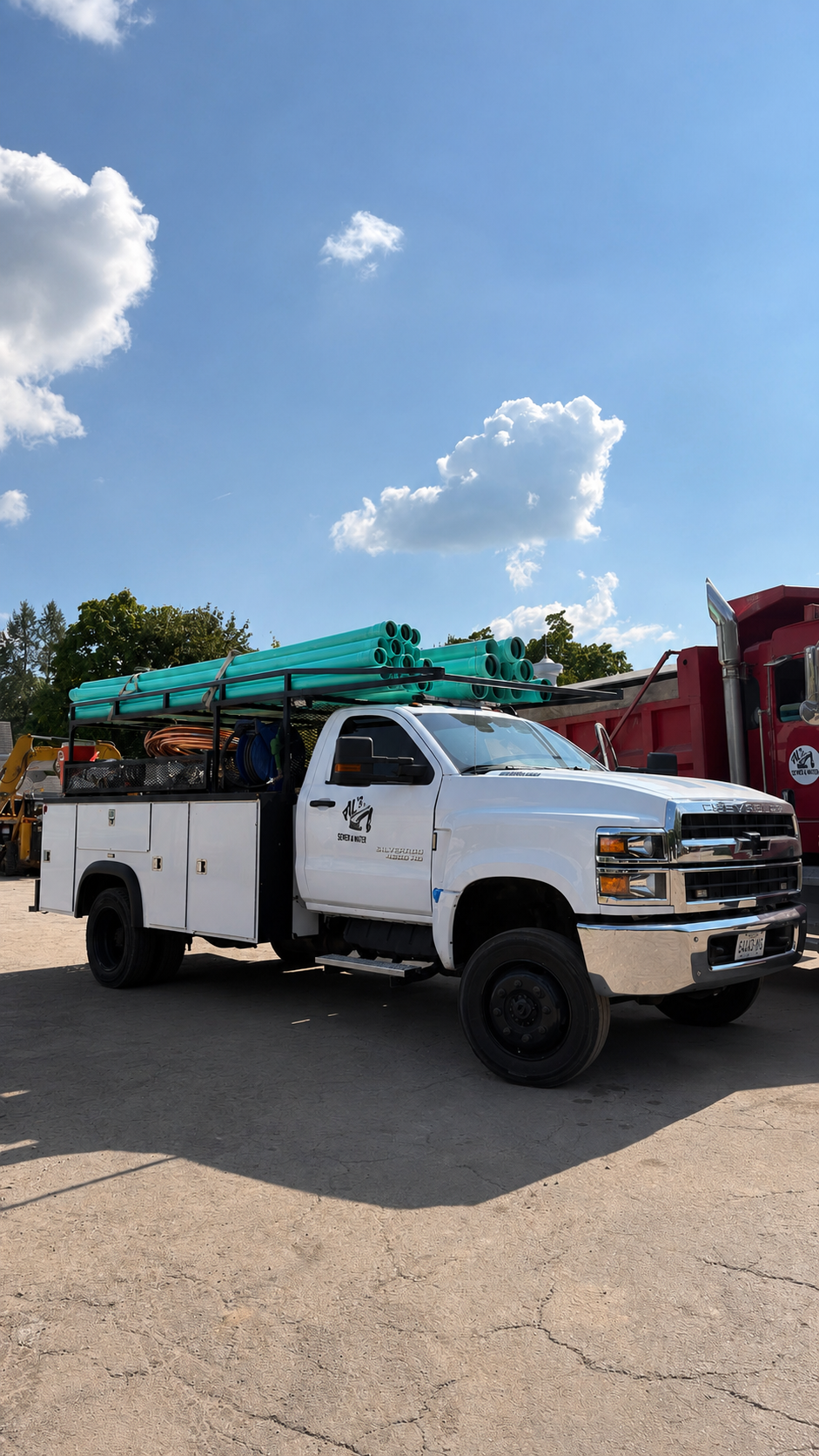 A white utility truck with teal pipes and orange hoses loaded on it, parked outdoors on a sunny day with blue sky and clouds.