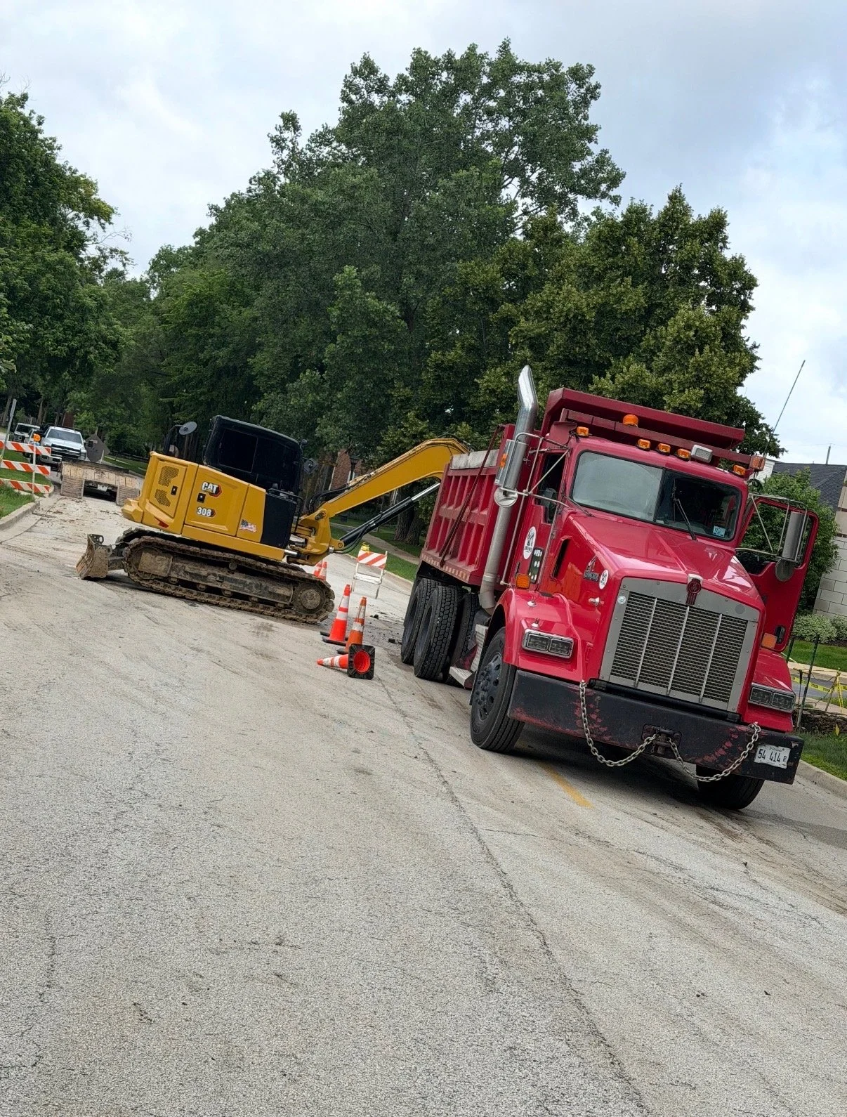 A red dump truck and a yellow excavator parked on a construction site with traffic cones and construction barriers.