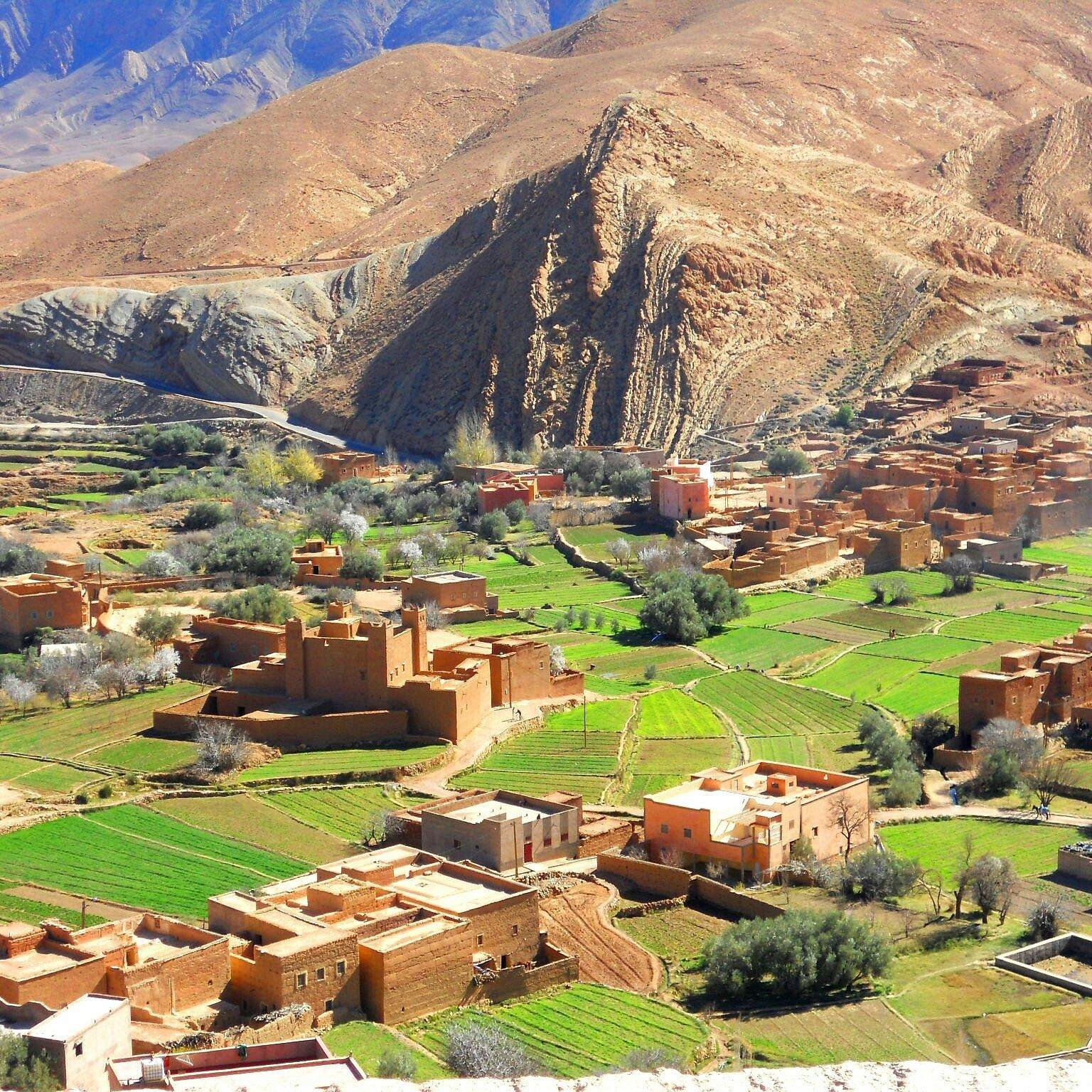 A small town in a valley surrounded by desert mountains, with green fields and trees.