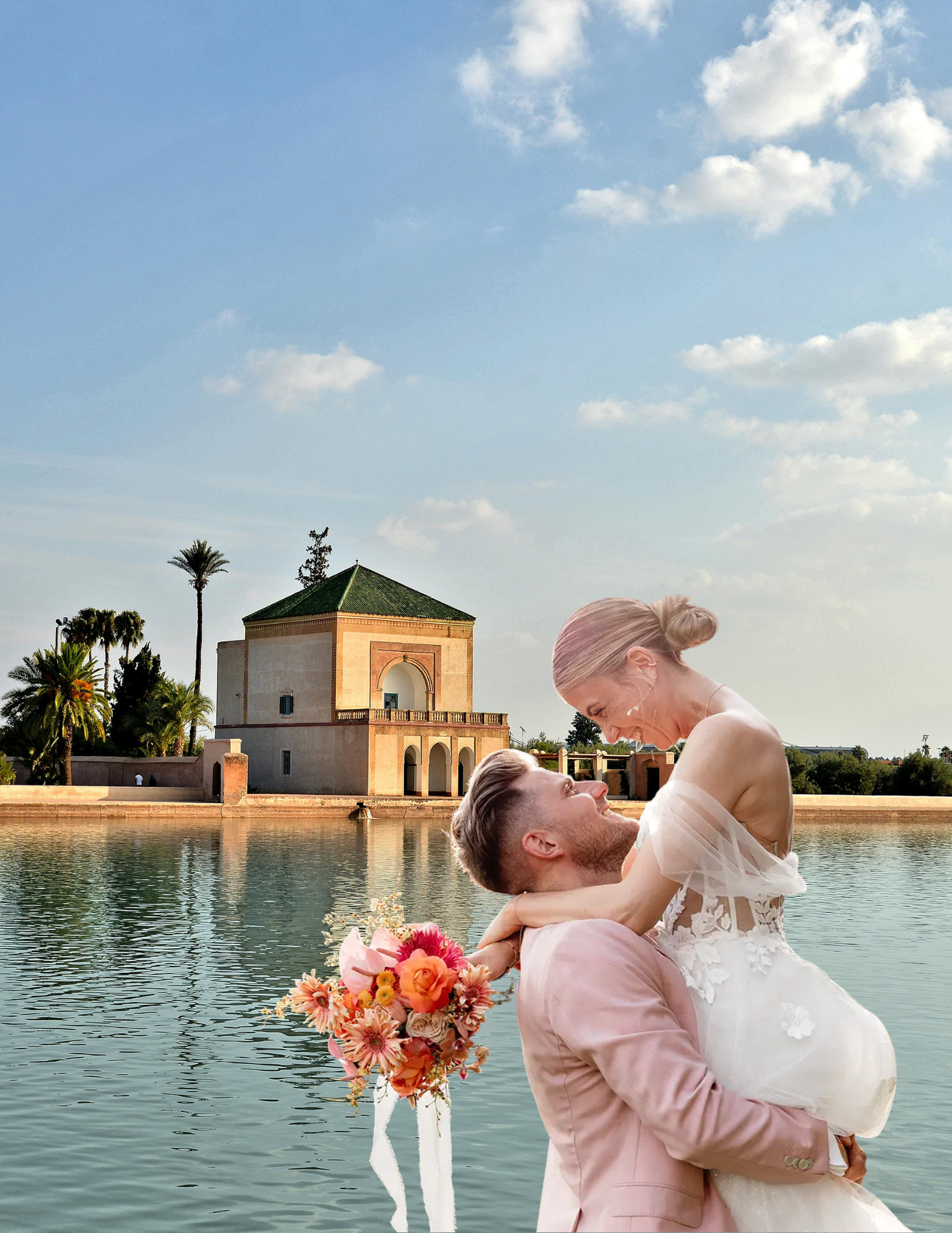 A newlywed couple is embracing on a lake with a historic building in the background. The bride is wearing a white wedding gown and holding a colorful bouquet of flowers, while the groom is dressed in a light pink suit.