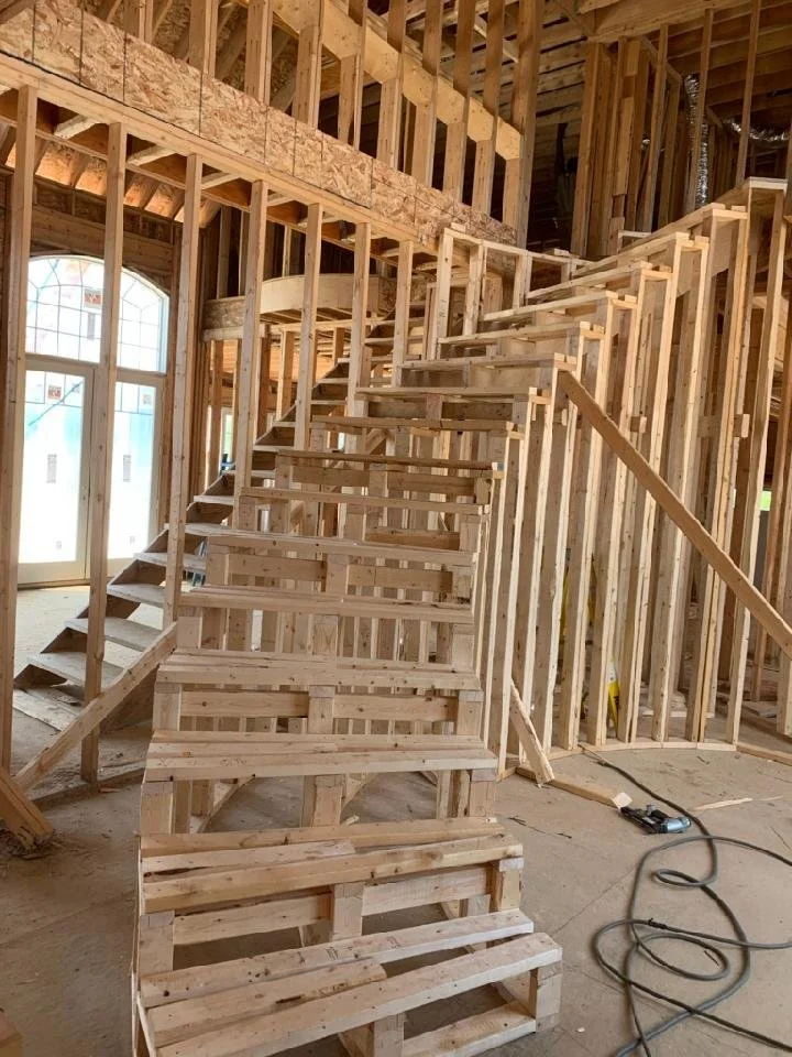 Intricate rough-in carpentry by Booras Builders showcases a complex curved staircase structure completely framed with wood risers, set within an open multi-story residential framing layout with exposed wall studs.