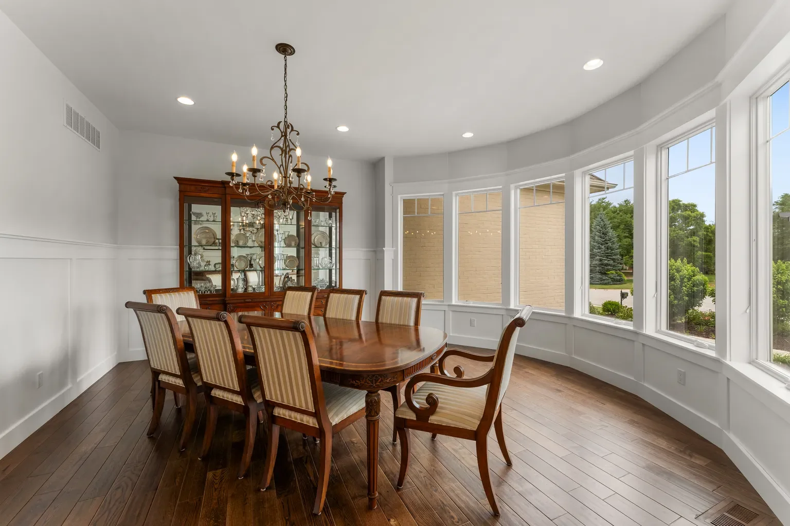 This Porter County dining room has a unique chandelier with lights that look like candles, rustic hardwood flooring, and large windows that gives the room a beautiful view at the lush backyard.
