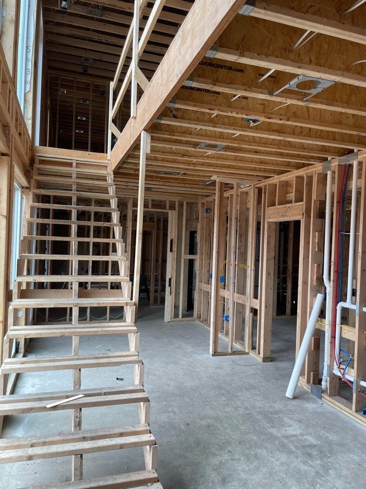 Interior of a house in Chesterton under construction with exposed wooden framing, staircase, and unfinished walls. Exposed plumbing, with red and white pipes, can be seen inside the wall.