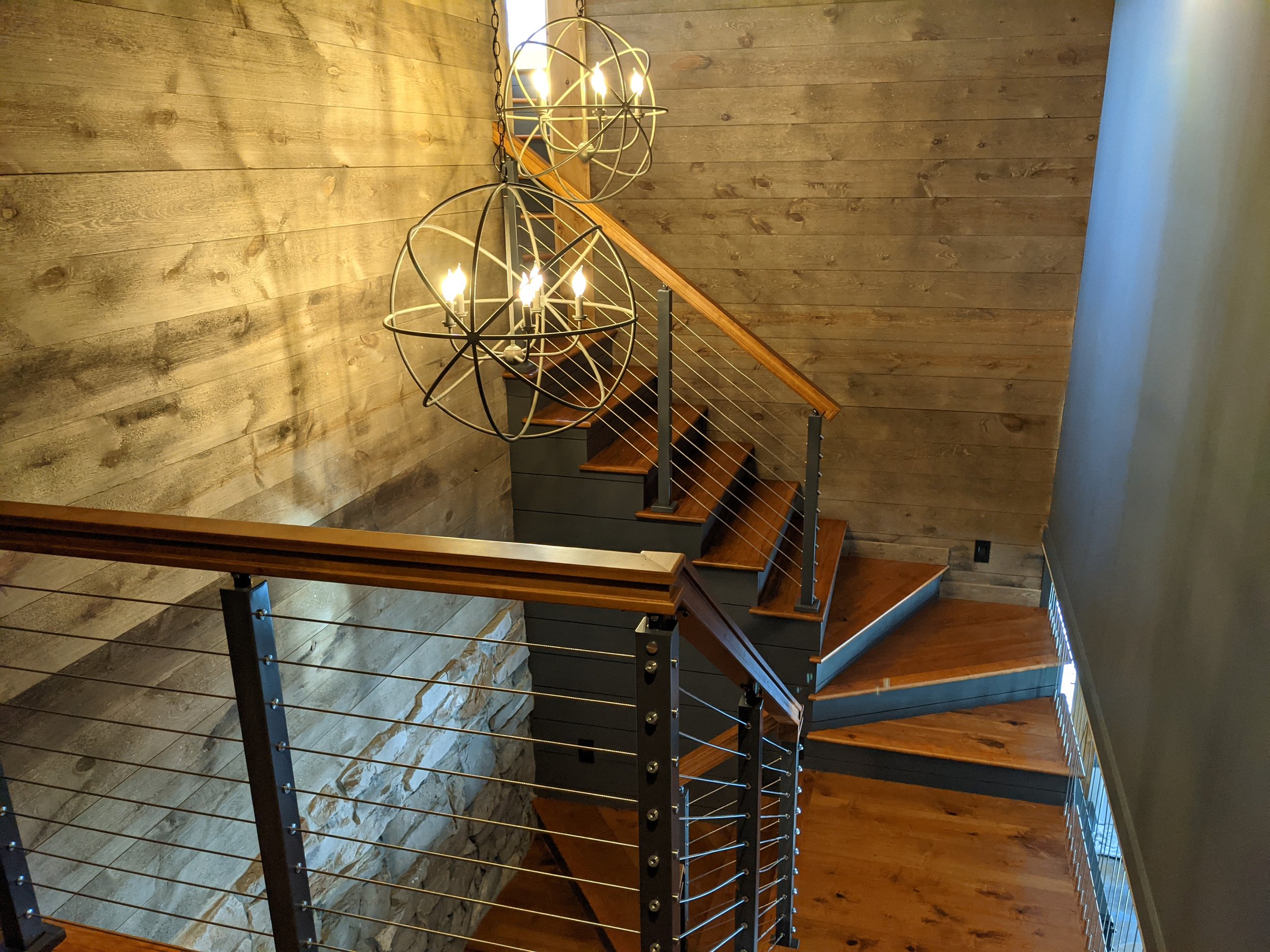 A modern wood staircase with underhead lighting and an orb chandelier in a Chesterton, Porter County home built by Booras Builders, featuring a modern design popular across Northwest Indiana.