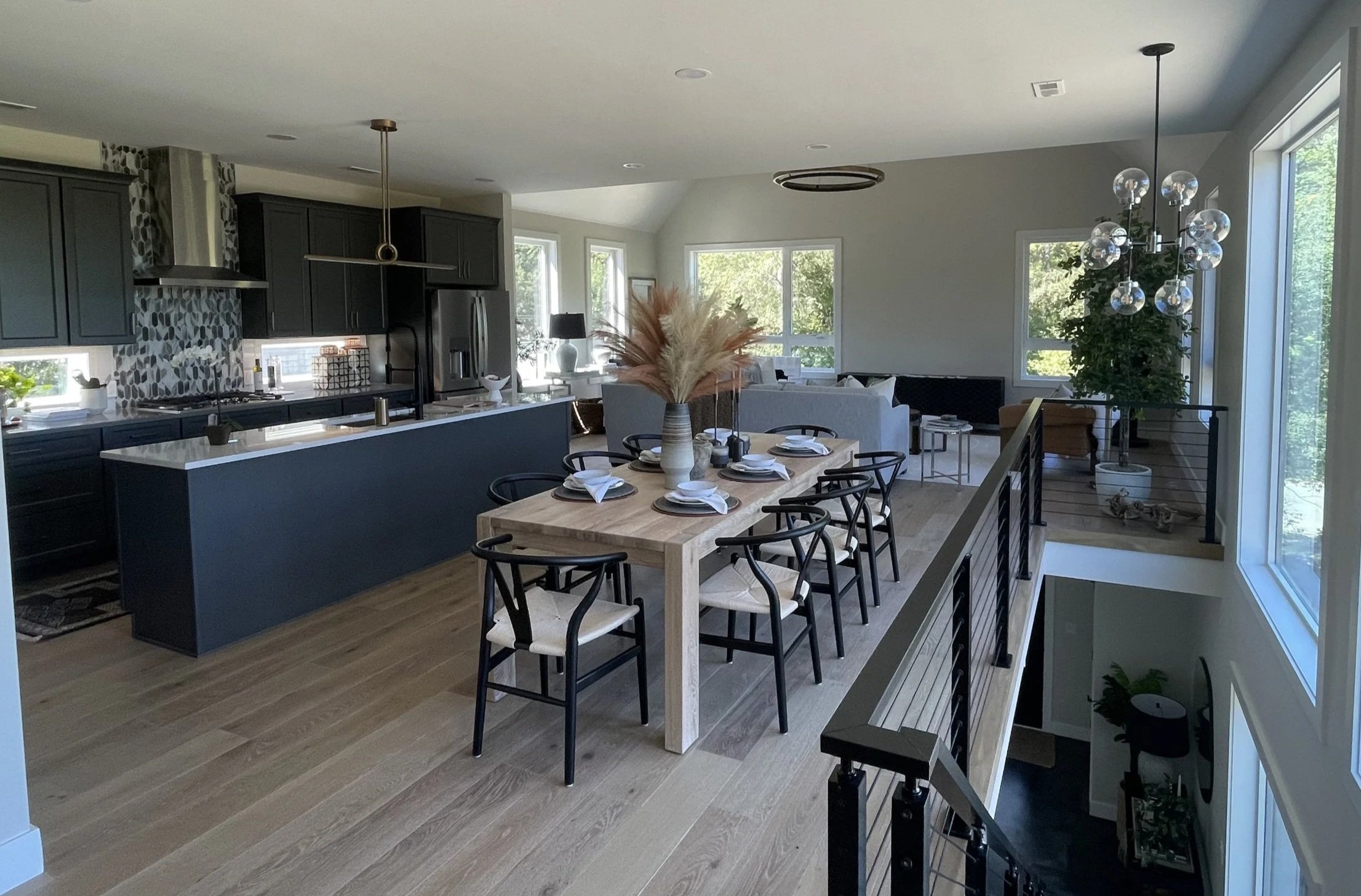 Modern open-concept kitchen and dining area with black cabinets, wood flooring, a large dining table set for six, and large windows letting in natural light—built for stylish living in Northwest Indiana.