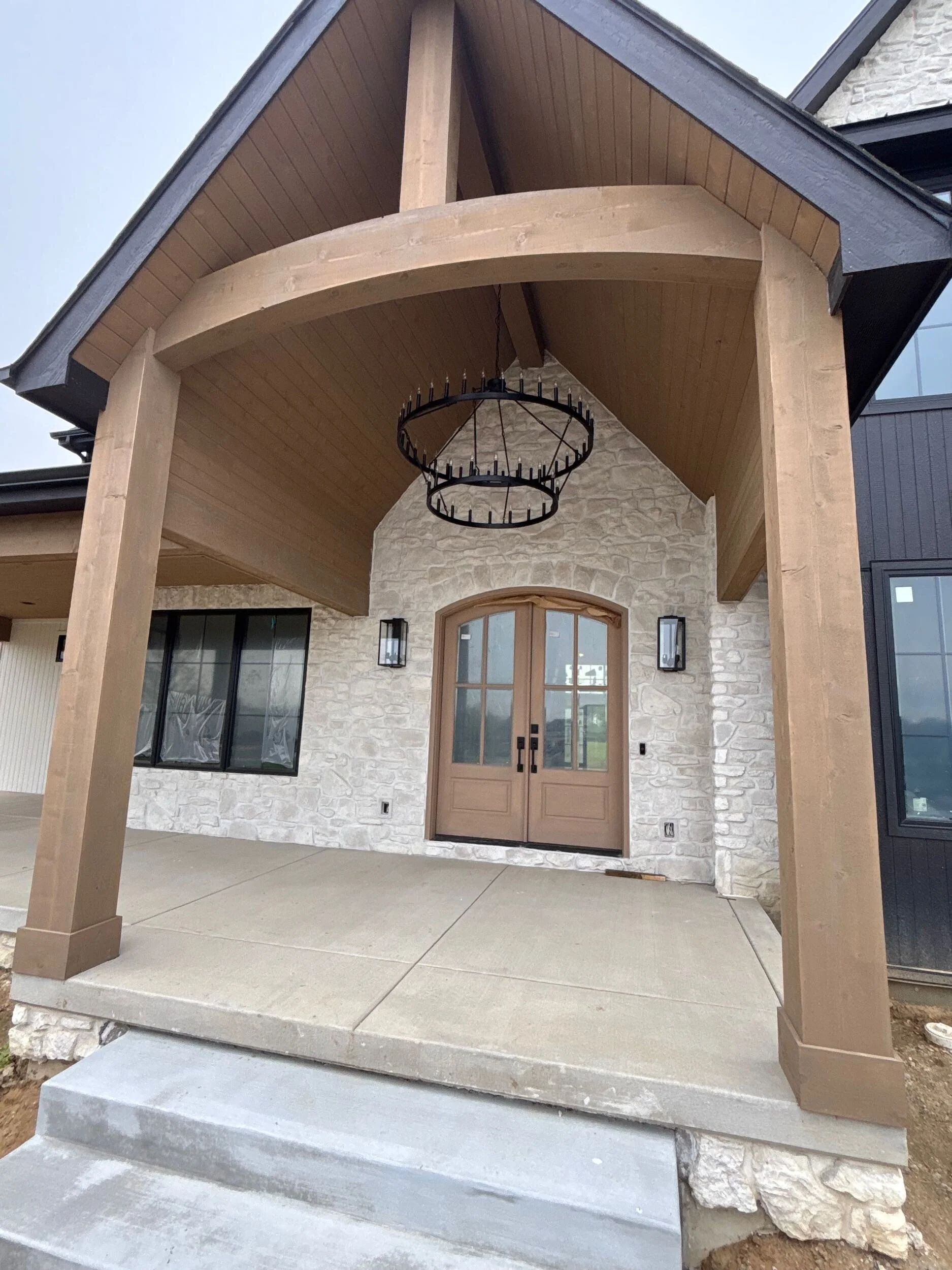 A Booras Builders custom built home with a beuatiful front porch with massive wood beams and luxury lights, as well as a custom wood entry door.