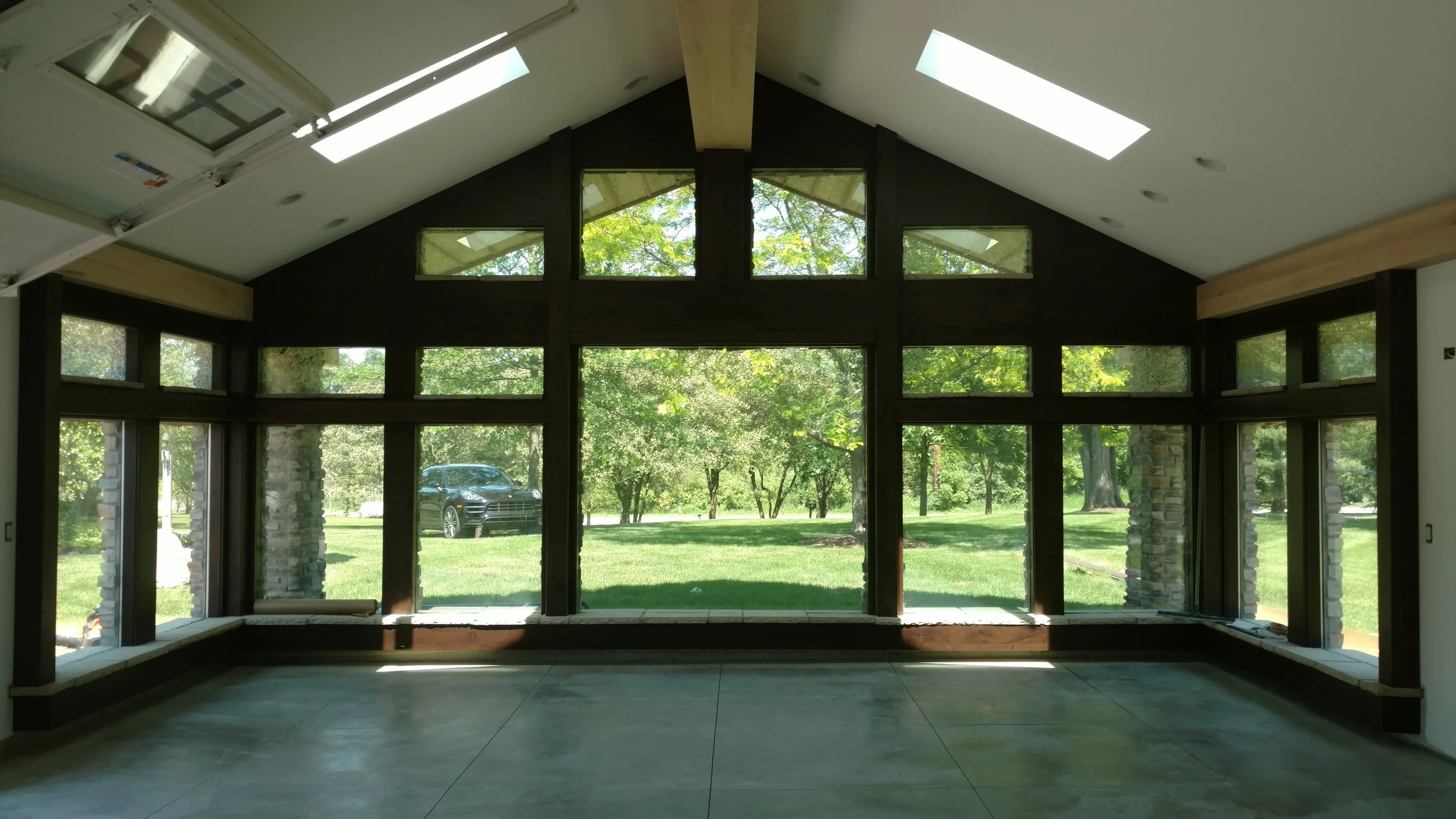 Constructed by the team at Booras Builders, this custom garage has polished concrete flooring, a dramatic vaulted ceiling with skylights, and floor-to-ceiling windows that provide panoramic views of the surrounding green landscape.
