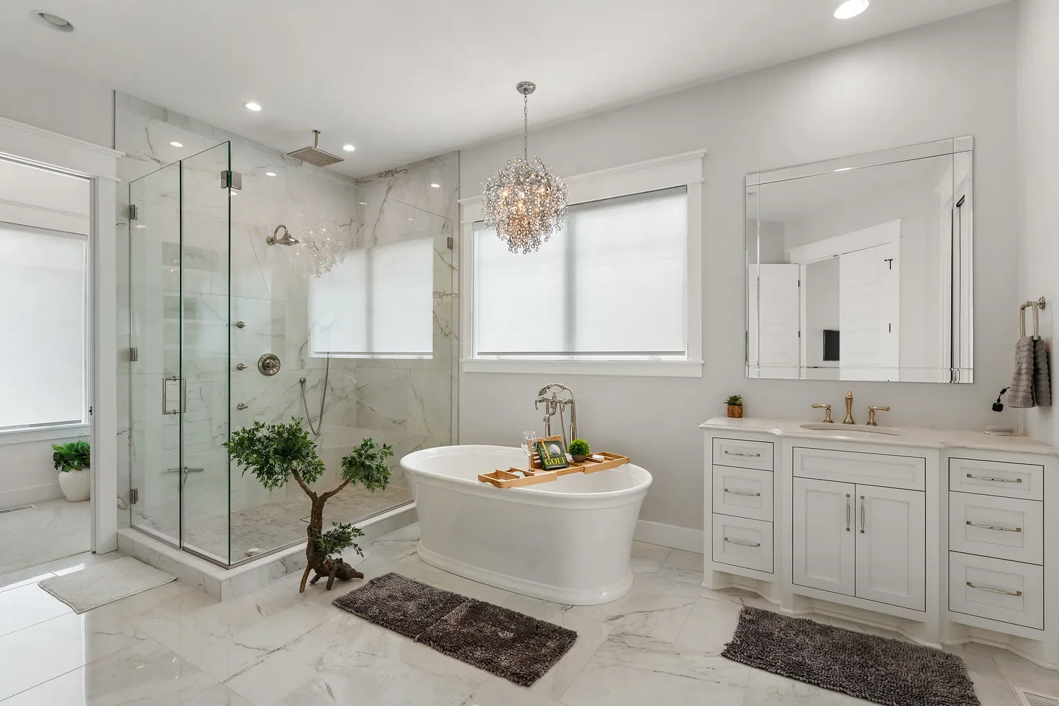 Crafted by Booras Builders, this luxurious Sand Creek bathroom balances function and high-end design with a white vanity, calacatta marble-style flooring, a glass walk-in shower, a standalone tub, and an elegant crystal fixture.