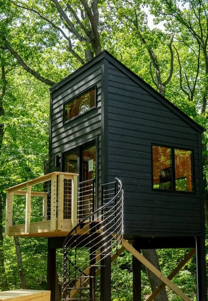 Situated in a forested area, this small cabin sits on stilts and was custom-built in Gary by Booras Builders. It's a contemporary version of a traditional treehouse; it has an intricate black and silver spiral staircase and sleek black siding.