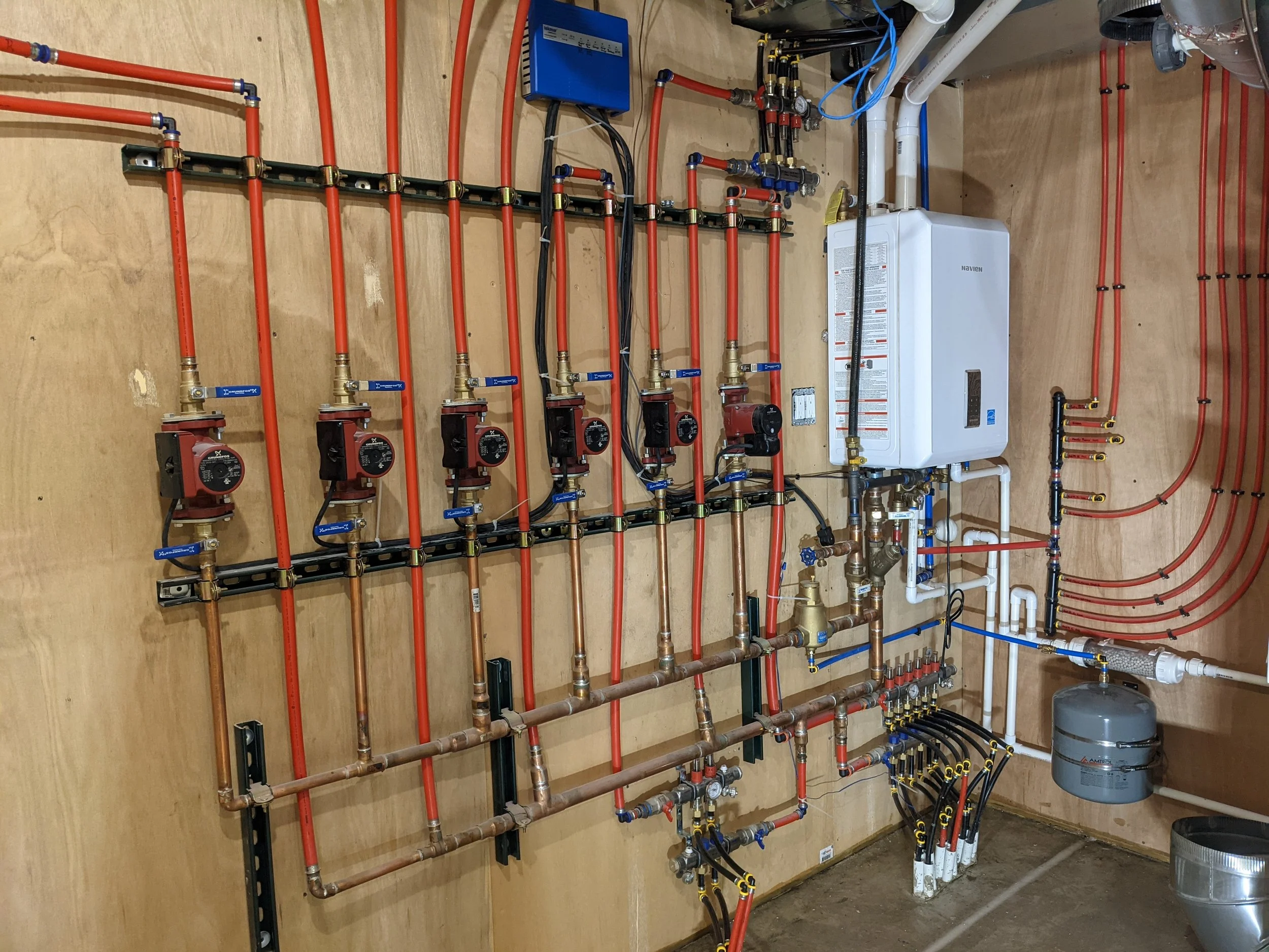 A highly detailed, professional mechanical system installed by Booras Builders, featuring a neat alignment of red tubing lines, copper pipes, and multiple circulation pumps for zoned residential hydronic heating in Porter County.