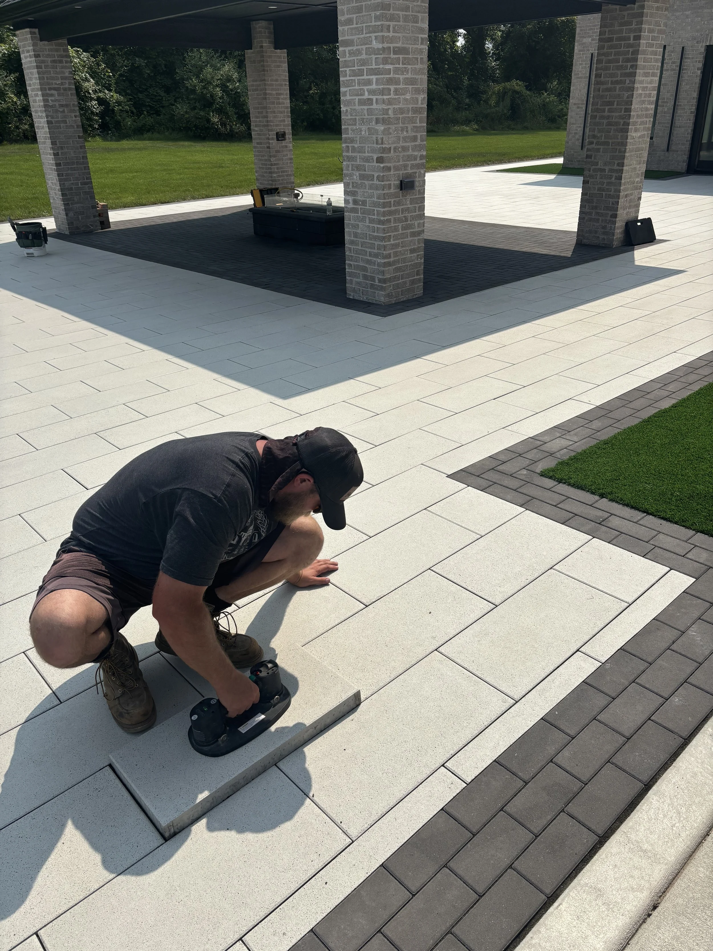 A man lowering the final paving tile in place for a white and gray tiled patio. This patio is part of the side yard of a home being built in Sand Creek by Booras Builders.