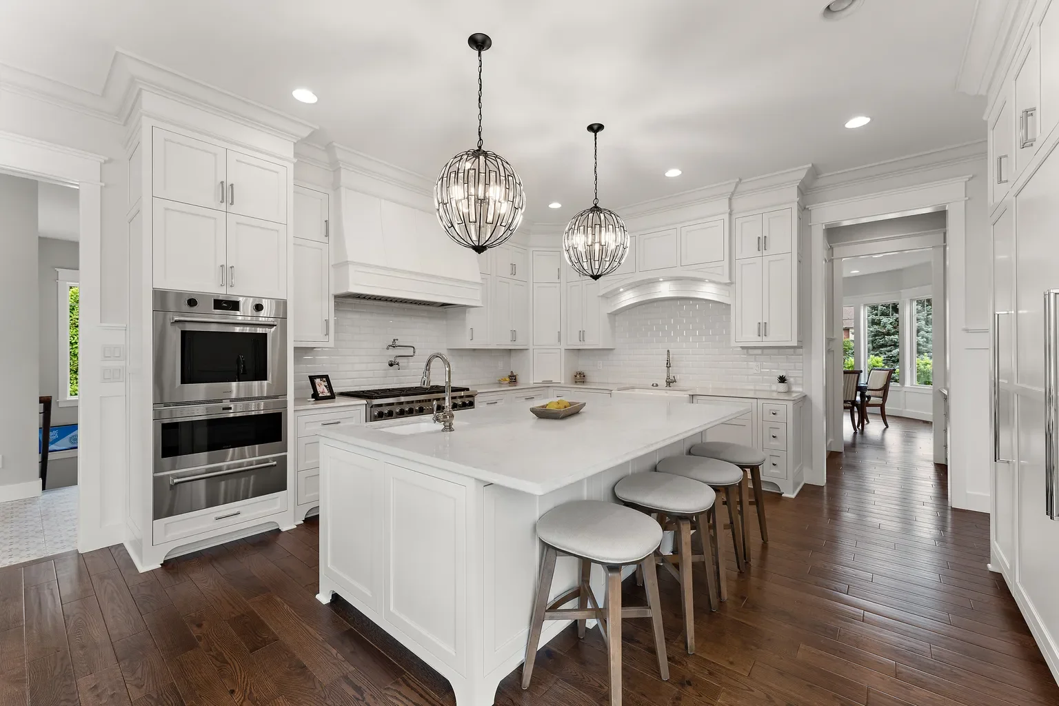 Upscale open-concept kitchen crafted by Booras Builders in Chesterton highlighting custom white floor-to-ceiling cabinetry, integrated crown molding, a massive central breakfast bar island, and premium built-in appliances over dark hardwood flooring.