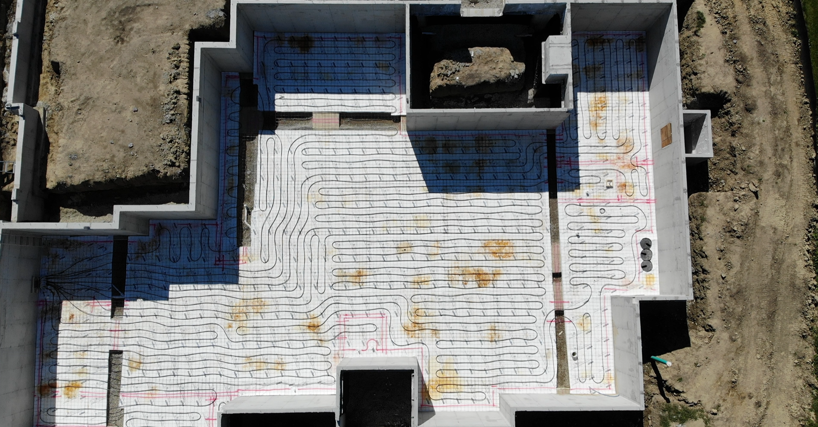 An overhead drone shot captures the precise layout of underfloor radiant heating PEX tubing installed over rigid foam insulation by Booras Builders, ready for a concrete floor pour within a new custom basement foundation.
