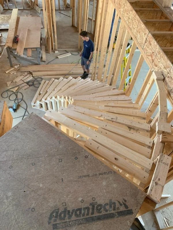 In Northwest Indiana, a Booras Builders carpenter reviews the intricate radius layout of a sweeping curved wooden staircase constructed with premium subflooring panels.