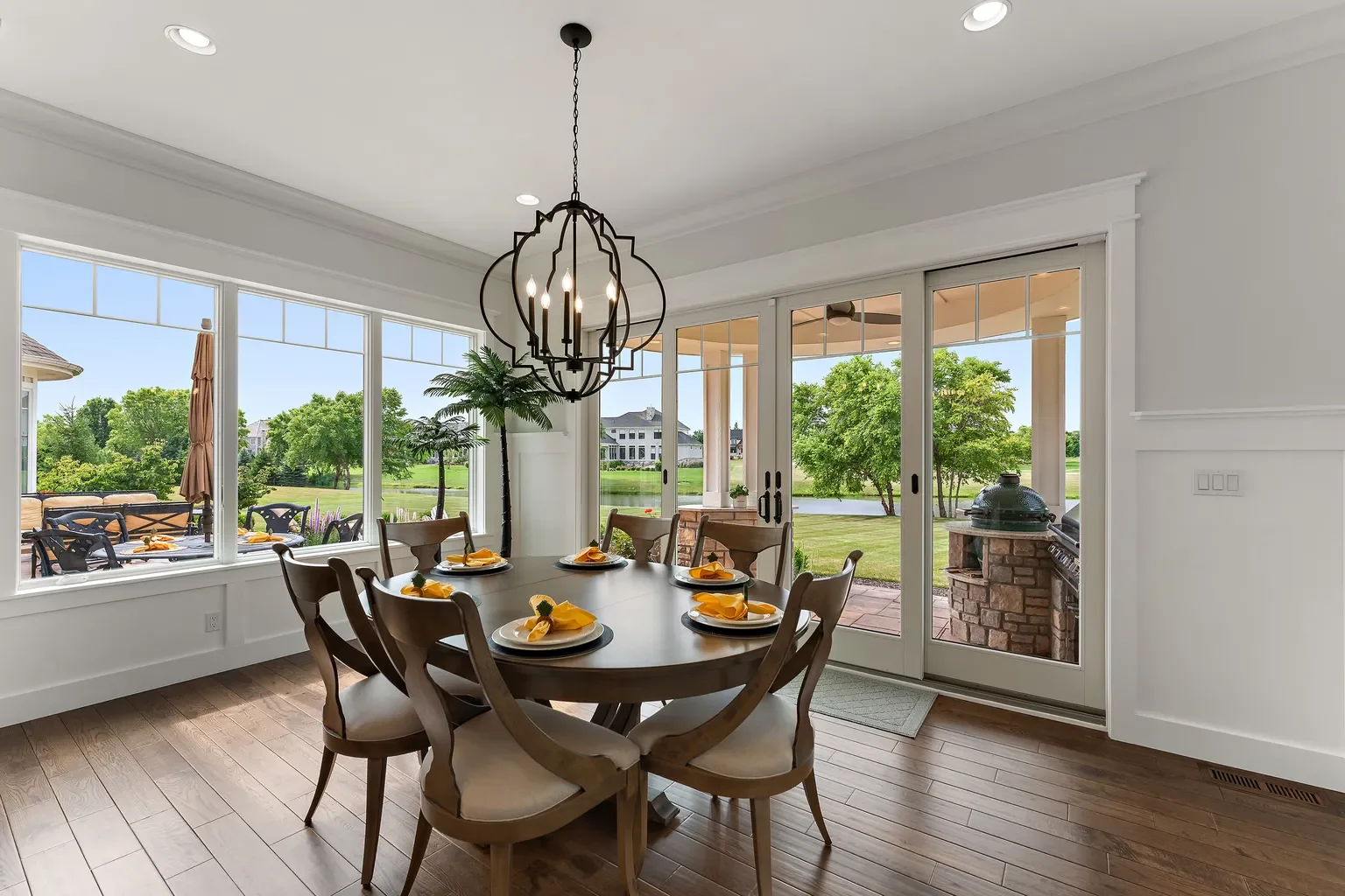 In Porter County, Booras Builders built a bright dining space with extensive wainscoting trim, panoramic windows, and large sliding glass doors opening to a scenic backyard view. In the dining room is a wooden table set for 6.