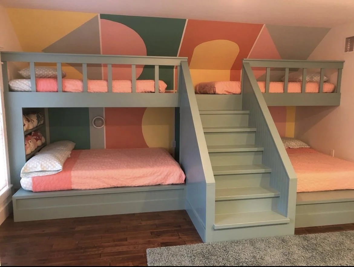 With integrated center stairs, protective safety rails, a muted green painted finish, and dark hardwood flooring, these custom built-in bunkbeds were meticulously constructed by Booras Builders and anchor a playful kids' bedroom.
