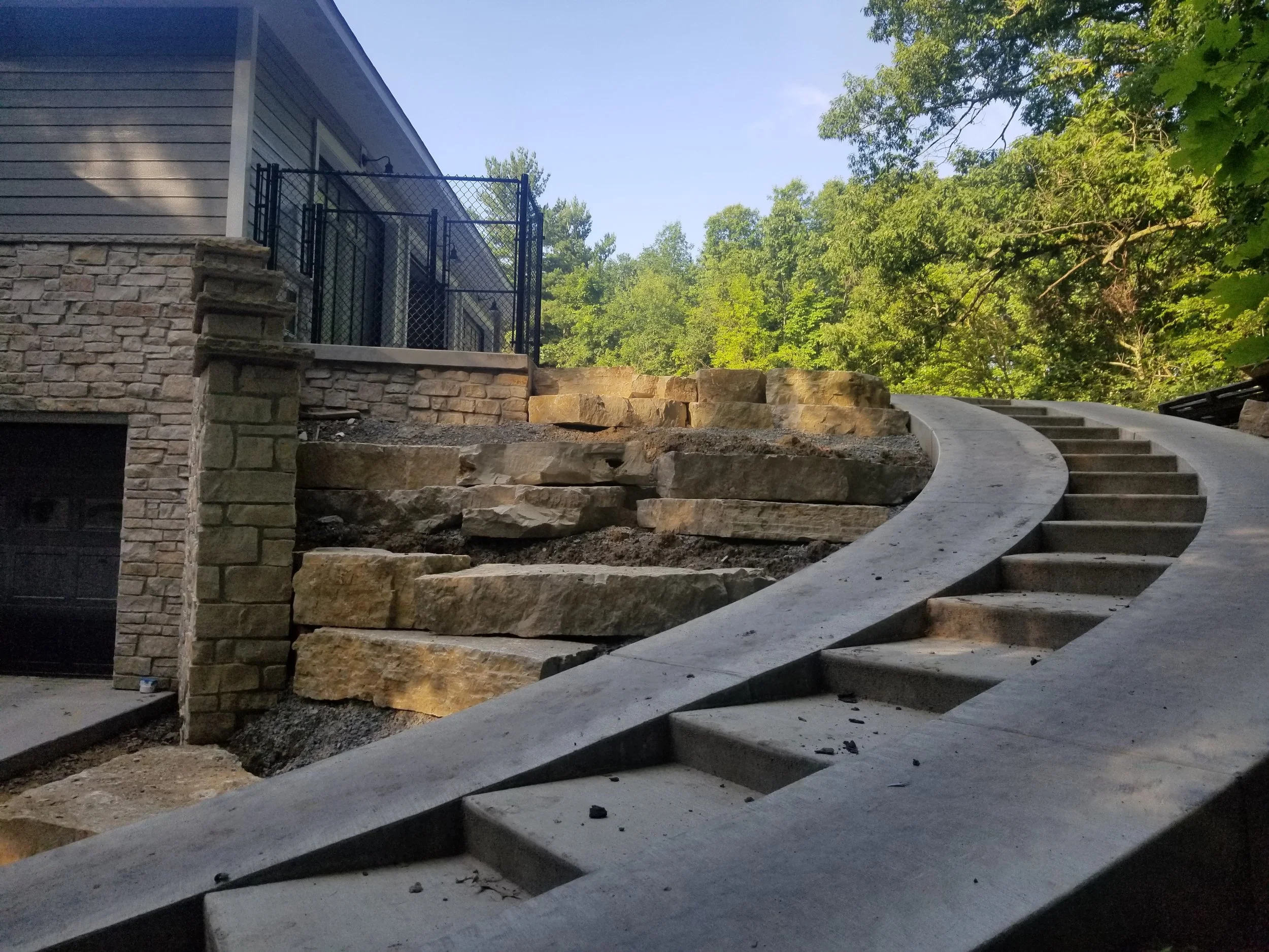This house in Porter County has a curved concrete staircase with a smooth built-in ramp sweeps alongside a massive natural stone retaining wall, highlighting a structural masonry feature that was added to this Booras Builders custom-built home.