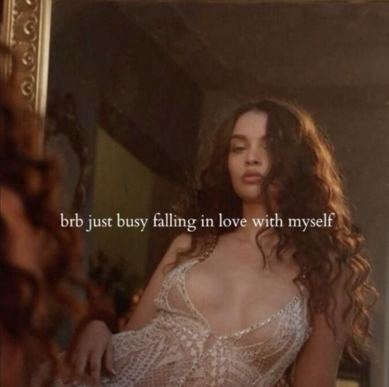 A woman with long curly hair is looking at a mirror, wearing a lace dress. There is a caption that reads 'brb just busy falling in love with myself'.